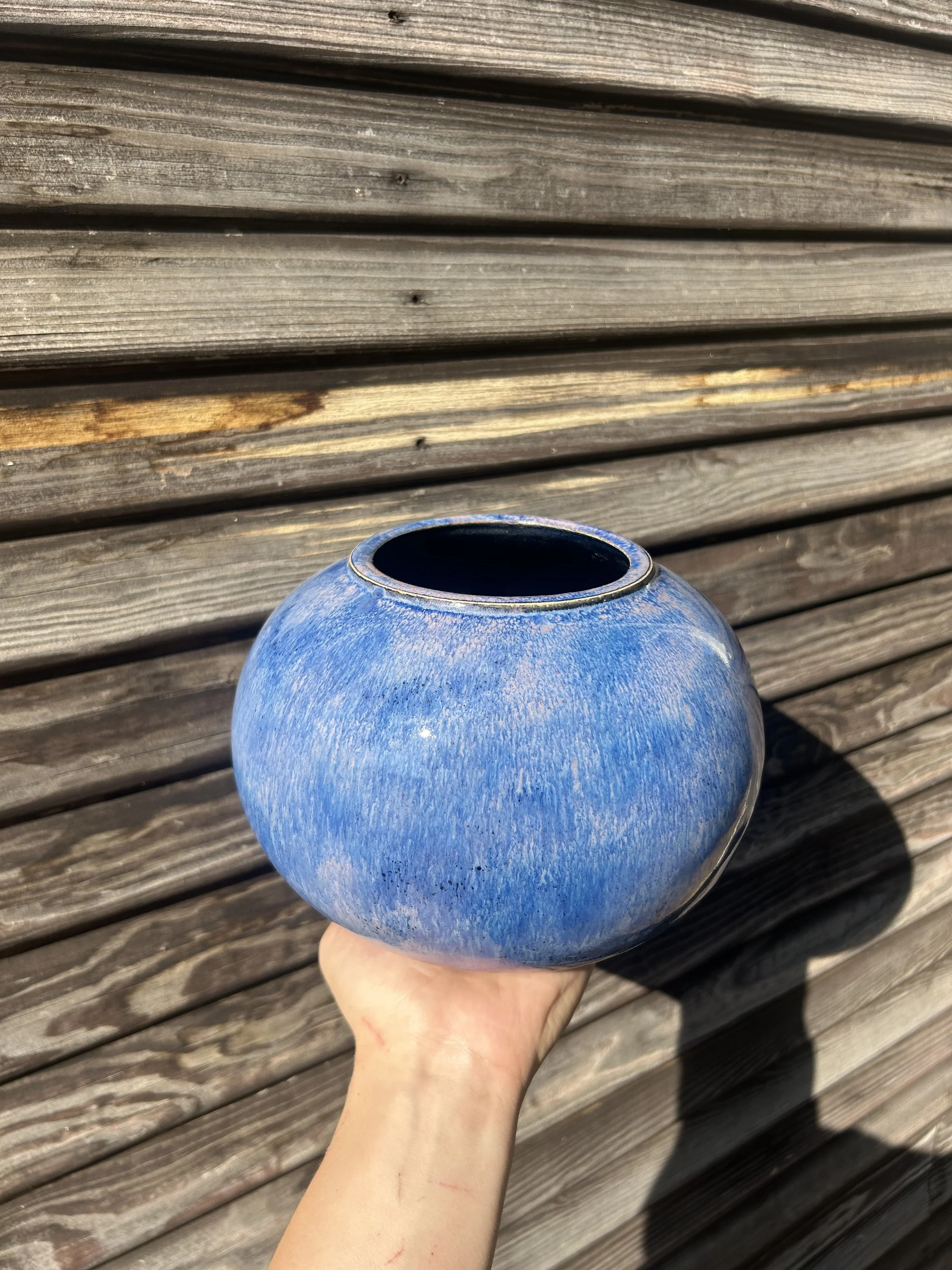 A blue ceramic vase held by a hand, against a background of weathered wooden planks.