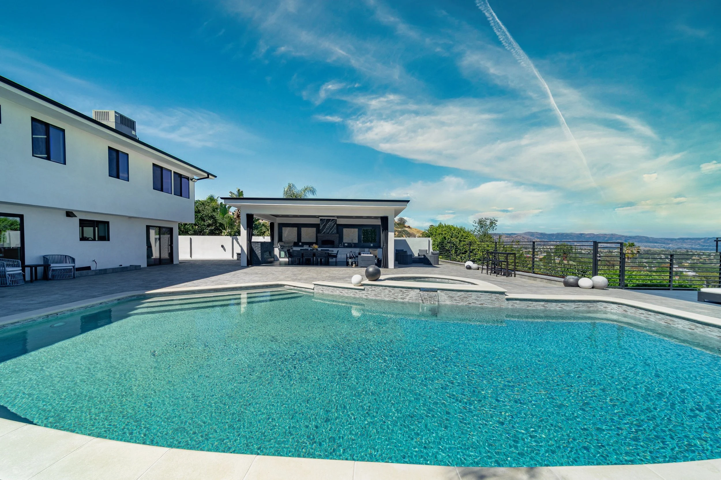 Modern house with outdoor pool, patio furniture, and scenic landscape view under partly cloudy sky.
