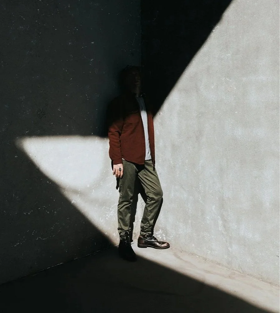 Person standing in a corner illuminated by a beam of sunlight, creating a contrast between light and shadow in the setting.