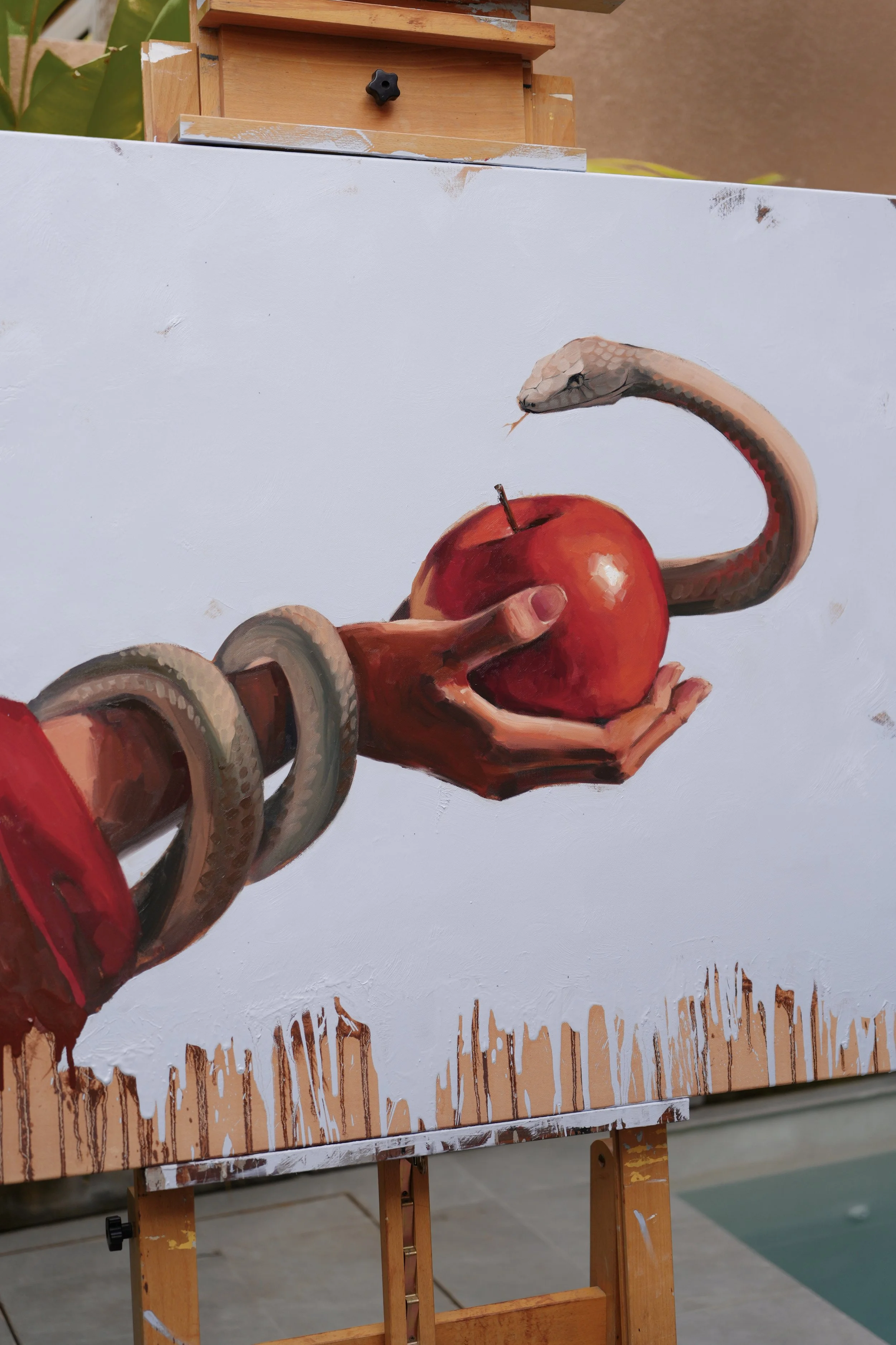 Sagwa on the easel in daylight – the hand, the apple and the snake above ochre drips, original oil on linen by Marina Ogai