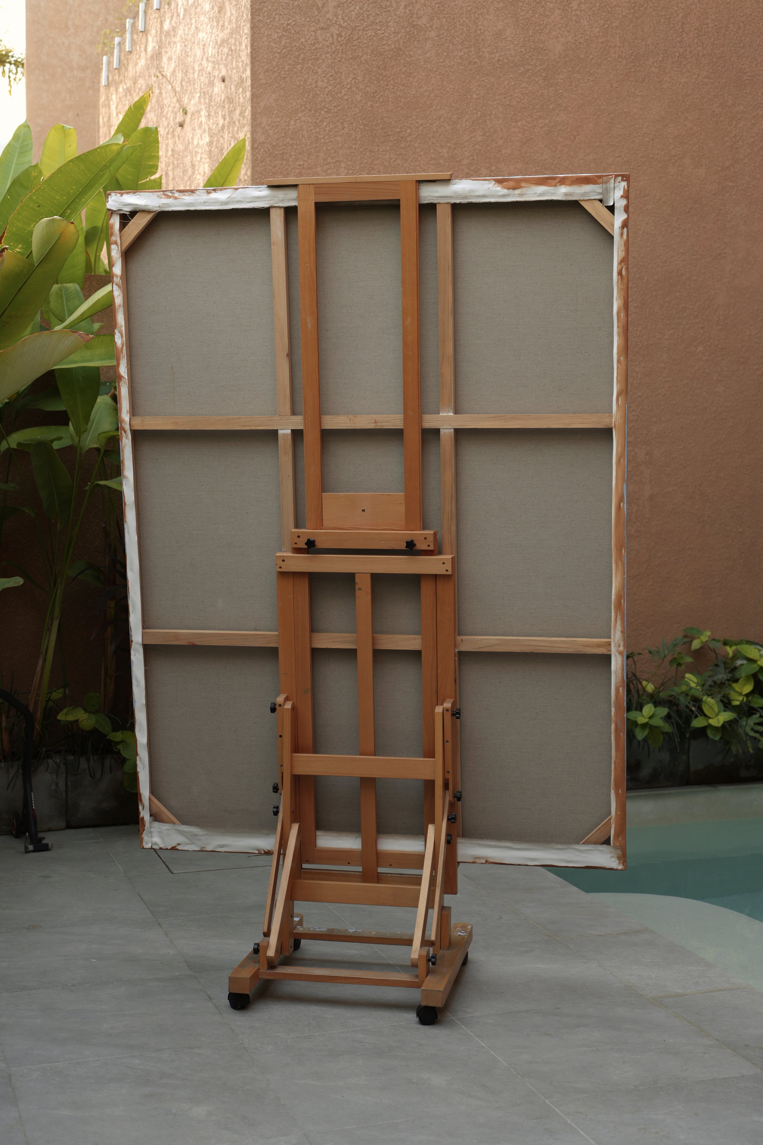 Back of a large linen canvas on a wooden easel in a garden studio, stretcher bars visible, work by Marina Ogai