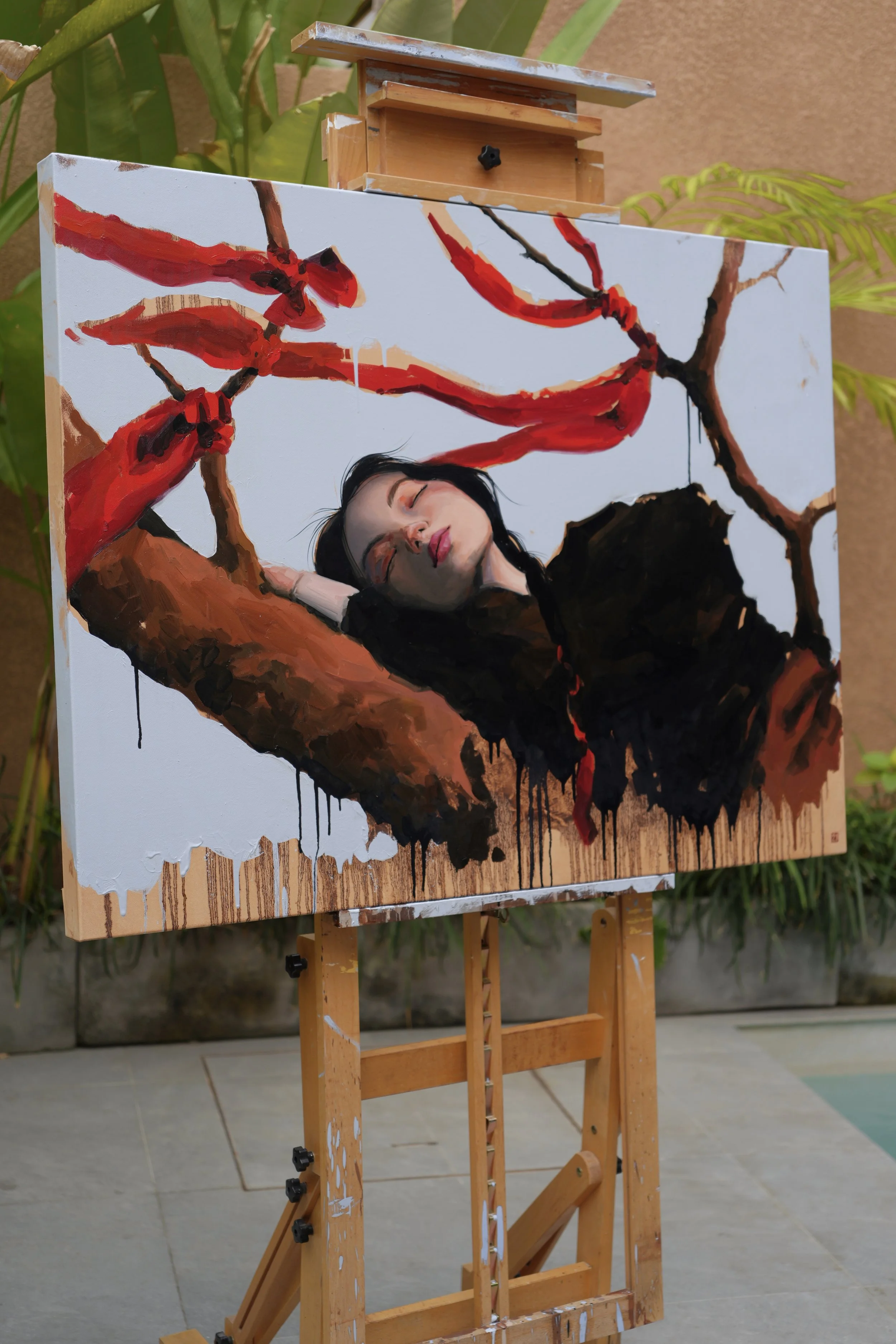Shinmok by Marina Ogai on an easel outdoors, a woman asleep on a branch with red ribbons, oil on linen canvas