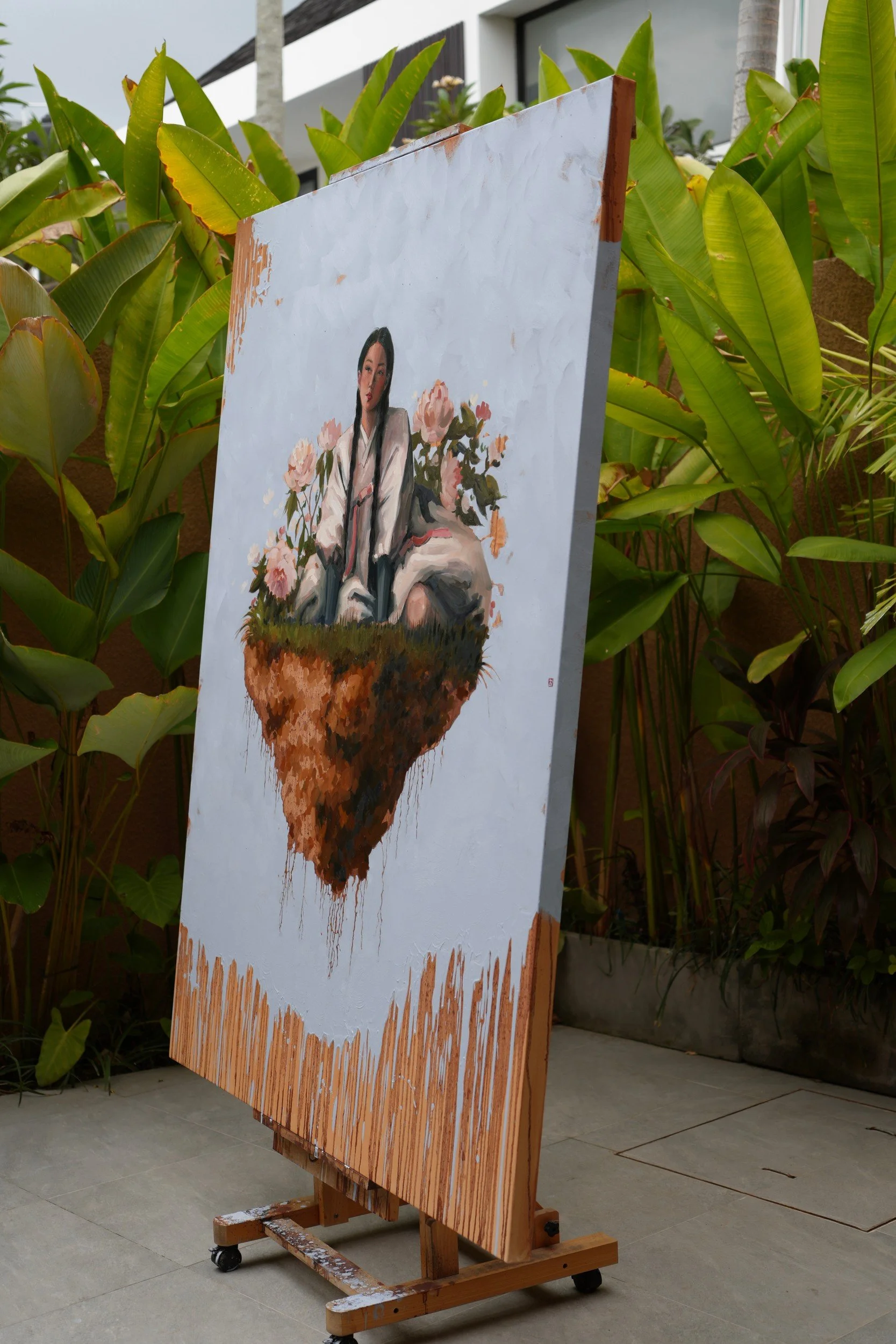 Moran by Marina Ogai – the large canvas on an easel outdoors, angled against tropical plants