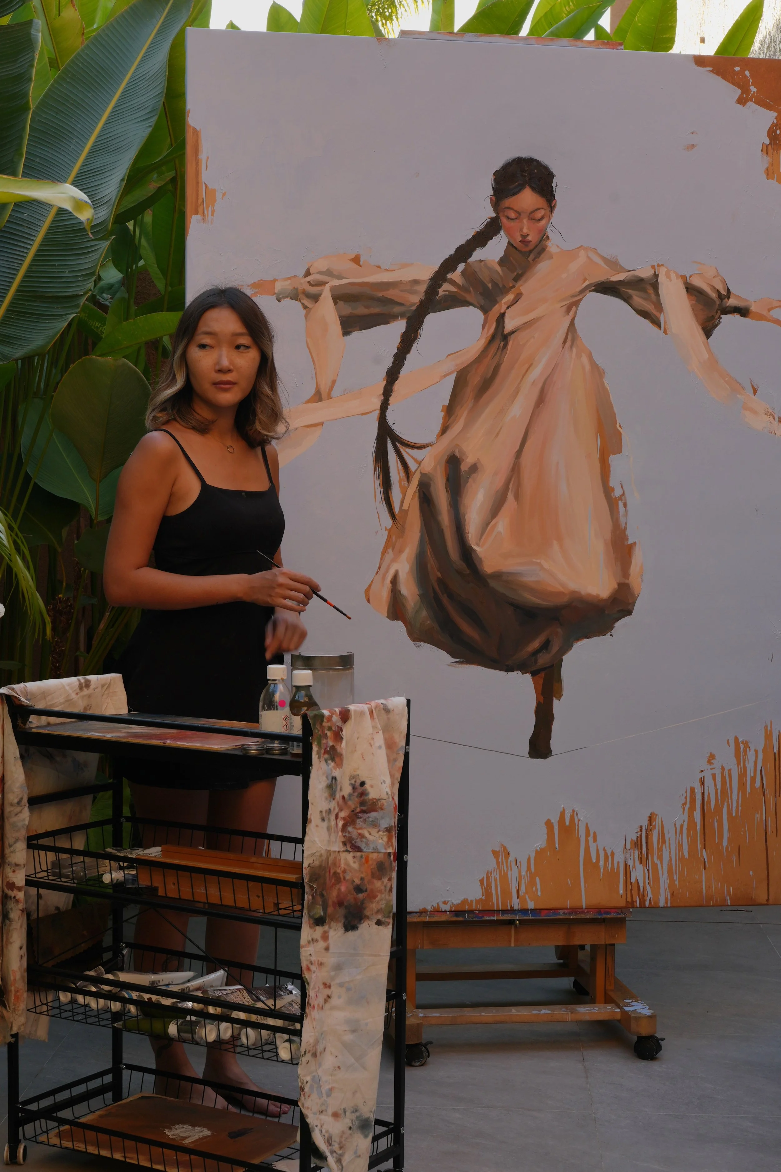 Marina Ogai with a brush beside her large oil painting of a girl in hanbok balancing on a line, from the series Given