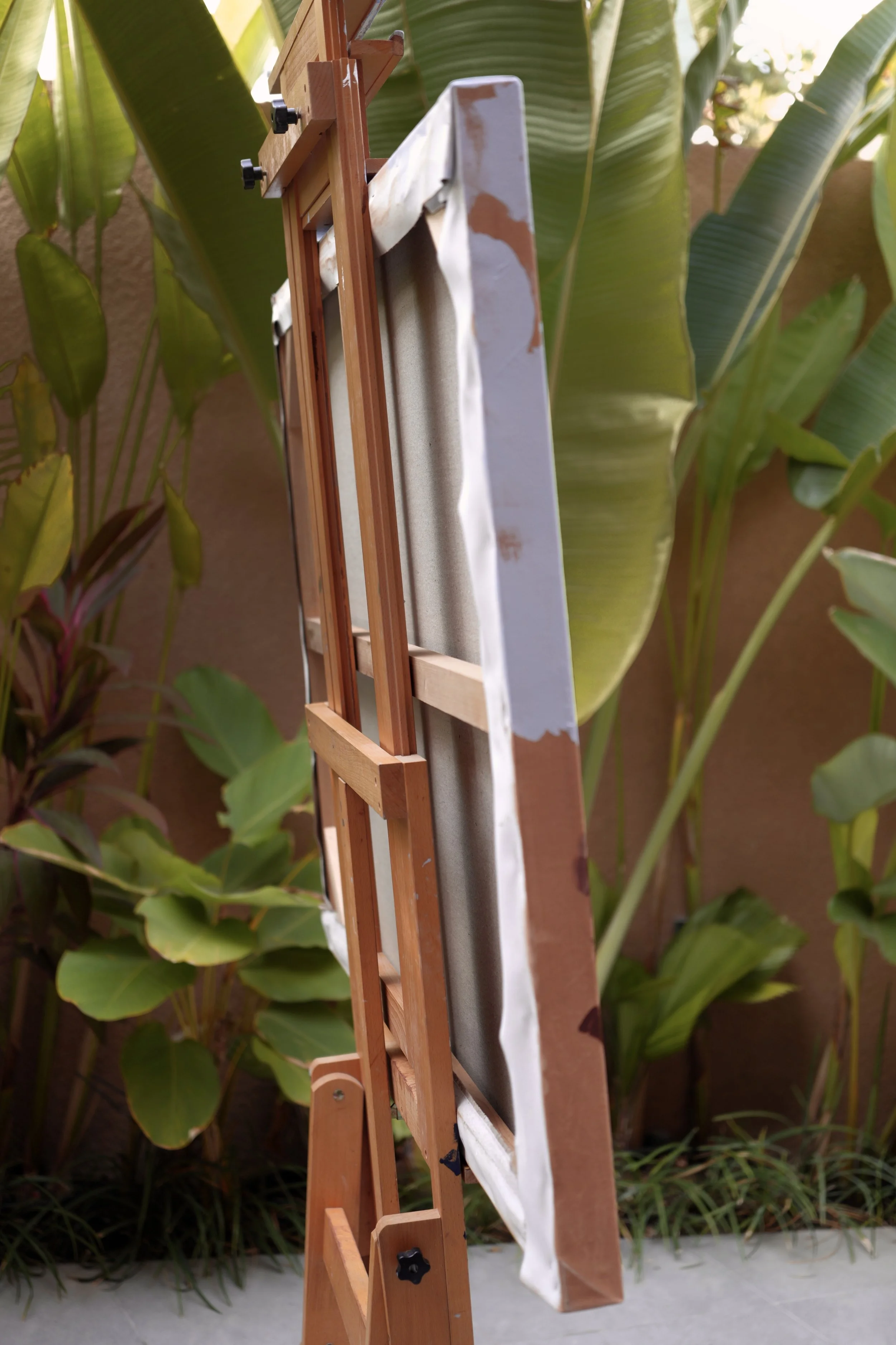 Sagwa seen from the side on the easel among tropical plants, showing the canvas depth, by Marina Ogai