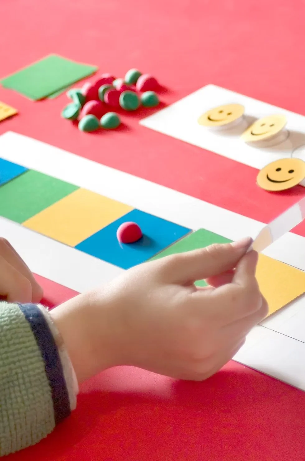 A person playing a colorful board game with smiley face tokens on a pink table.