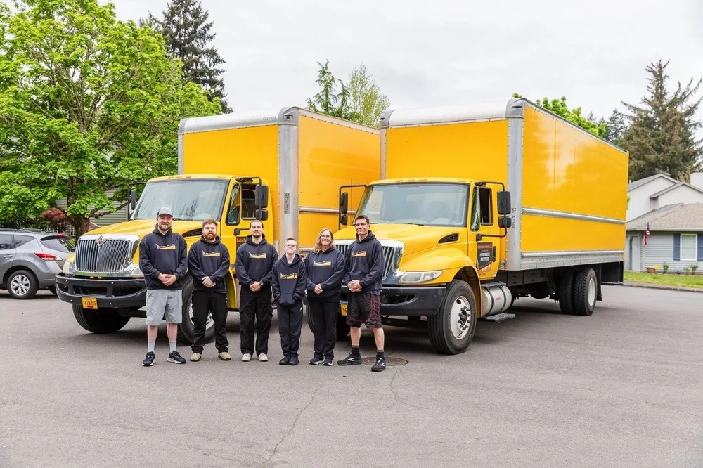 Butterfield team lined up in front of two yellow moving trucks, move in Newberg