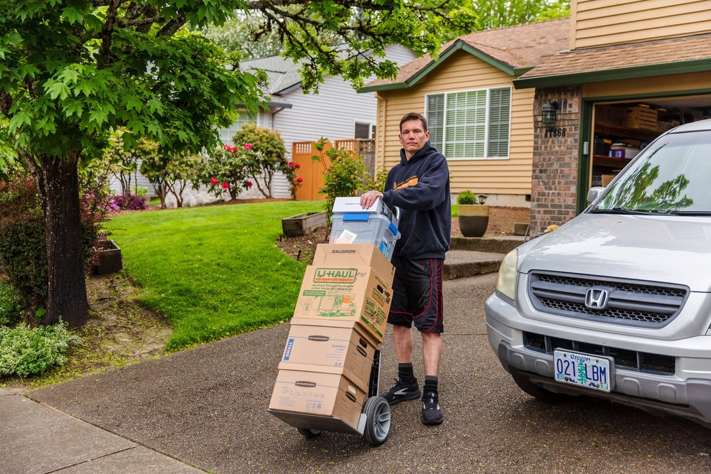 Mover wheeling a dolly of boxes down a suburban driveway, packing job in Beaverton