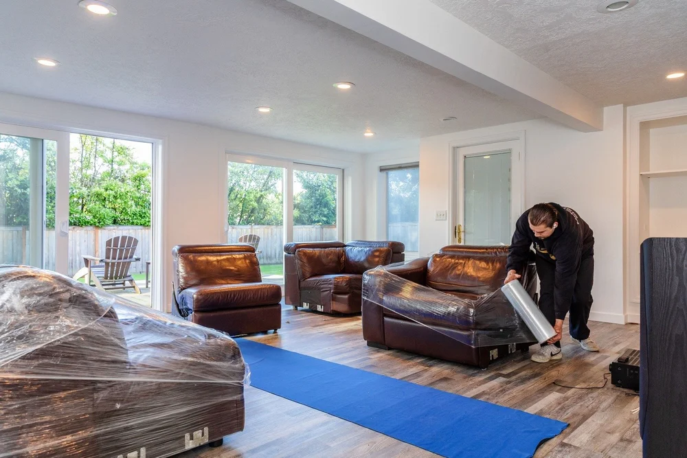 Mover protecting leather furniture with floor runners in a bright living room, senior move in Tigard