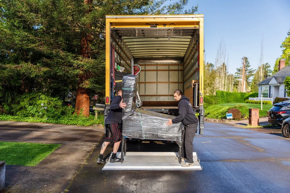 Two movers rolling a shrink-wrapped dresser onto the truck liftgate, move in Newberg