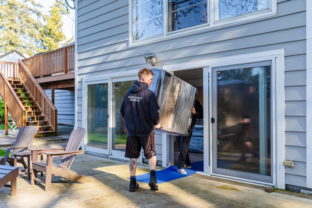 Mover carrying a wrapped piece out a back patio door onto a floor runner, move in Happy Valley