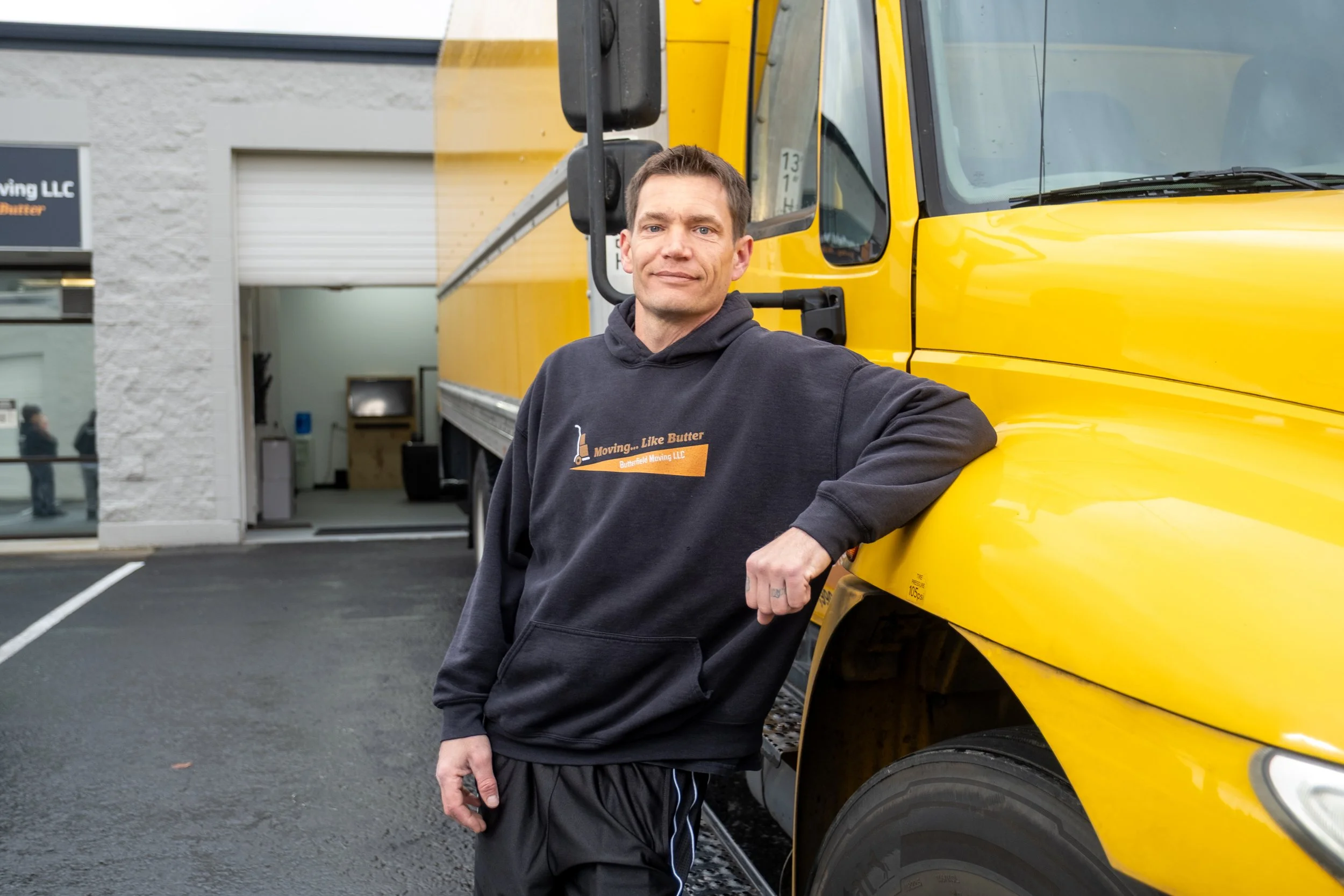 A man standing next to a large yellow moving truck parked outside a building.