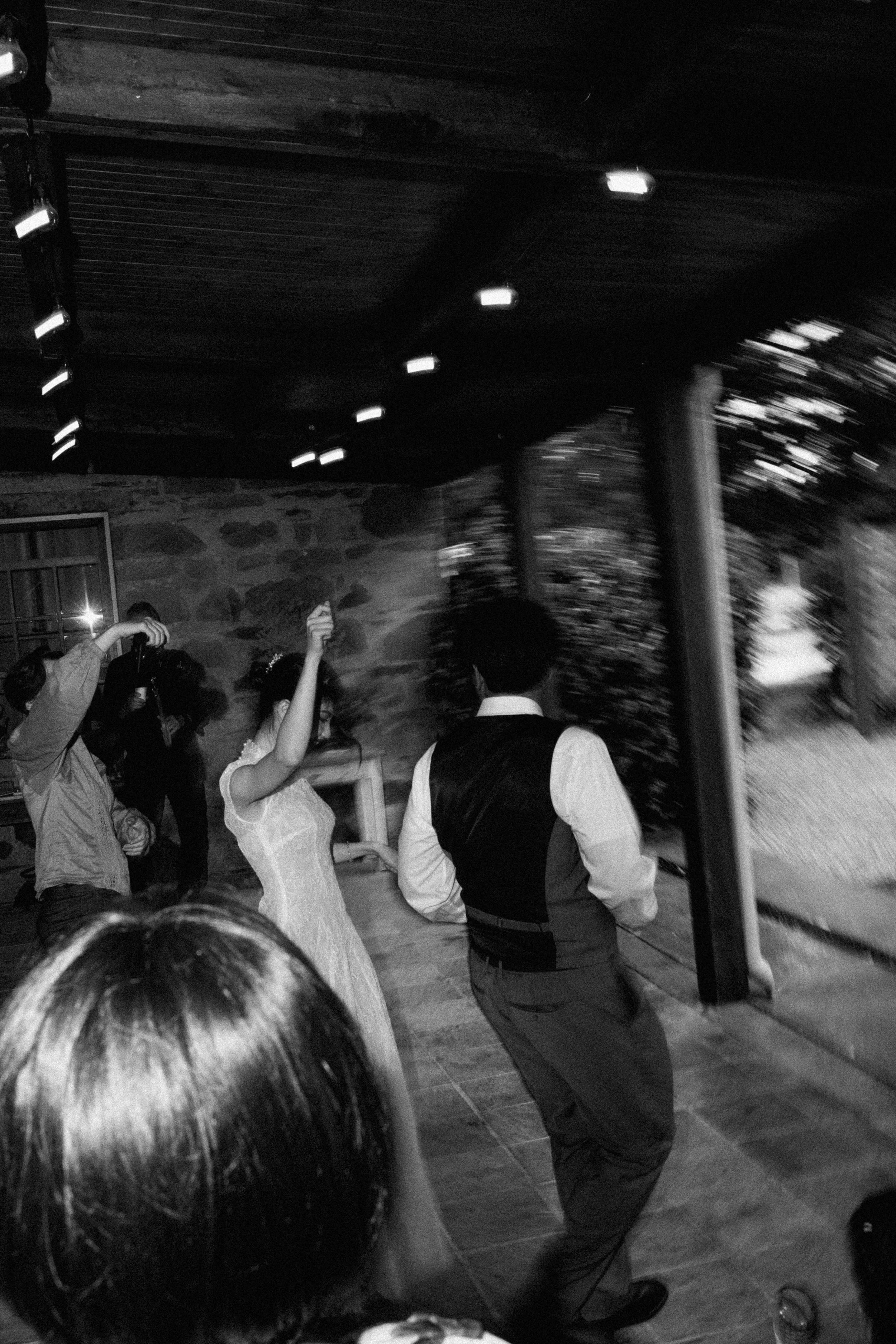 People dancing and socializing indoors, with a stone wall background and string lights on the ceiling.