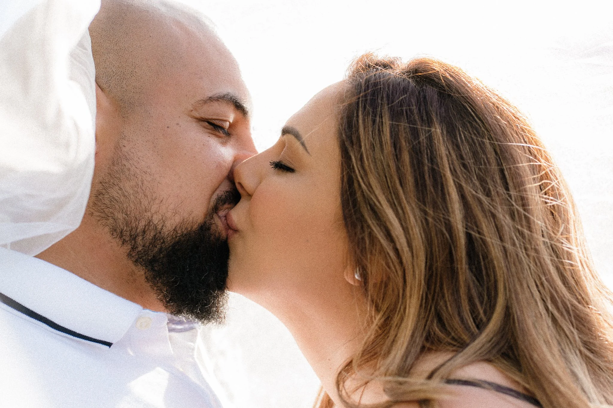 A couple about to kiss, with their noses touching and eyes closed, against a bright background.