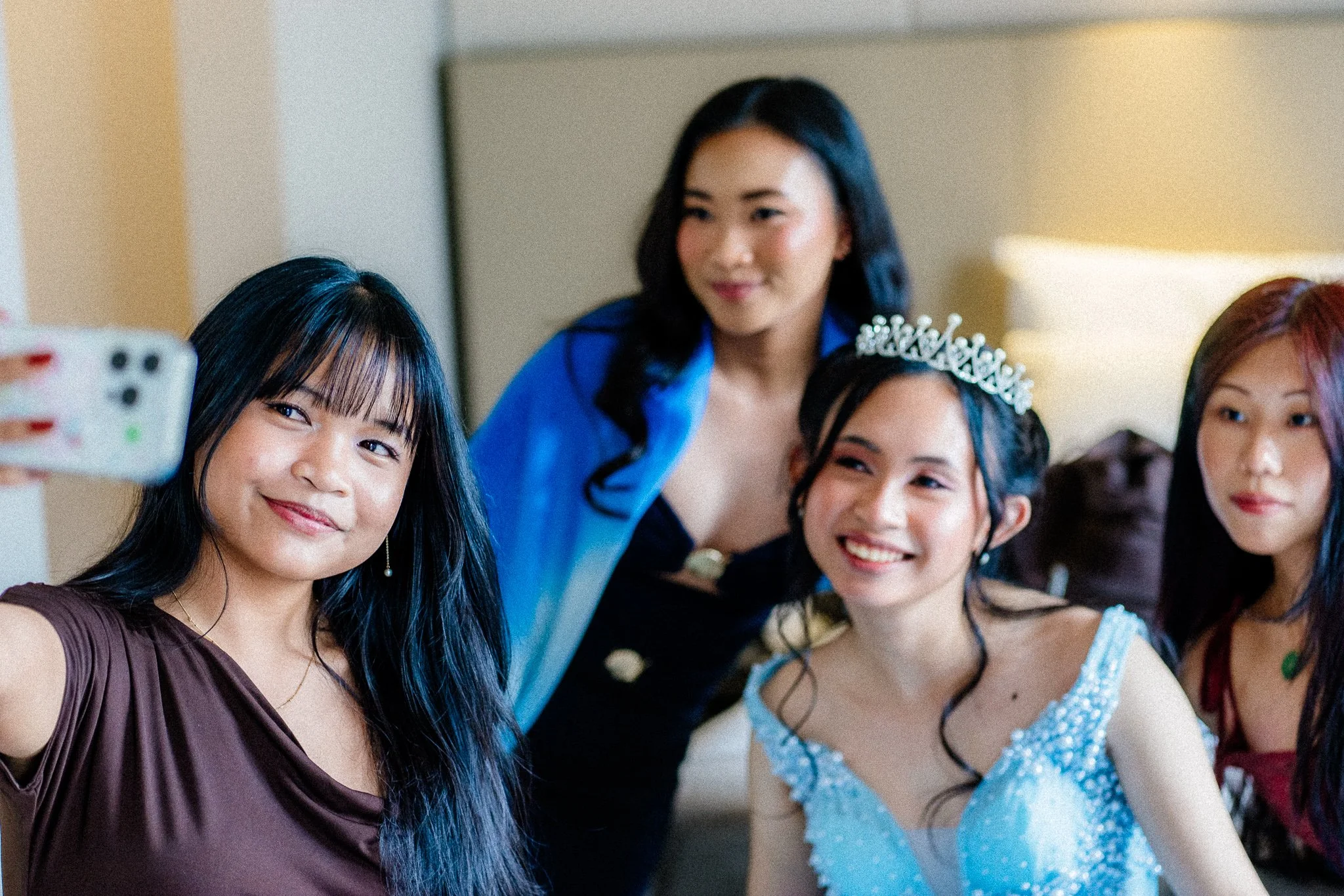 Group of young women taking a selfie at a celebration, one wearing a tiara, others in dresses, smiling.