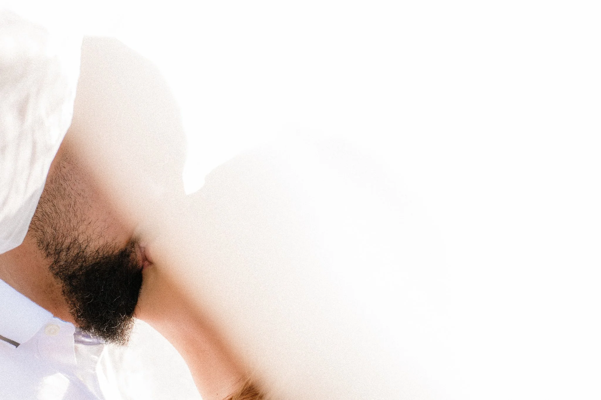 Close-up of a man's face with a beard, partially visible, wearing a white shirt with a button.