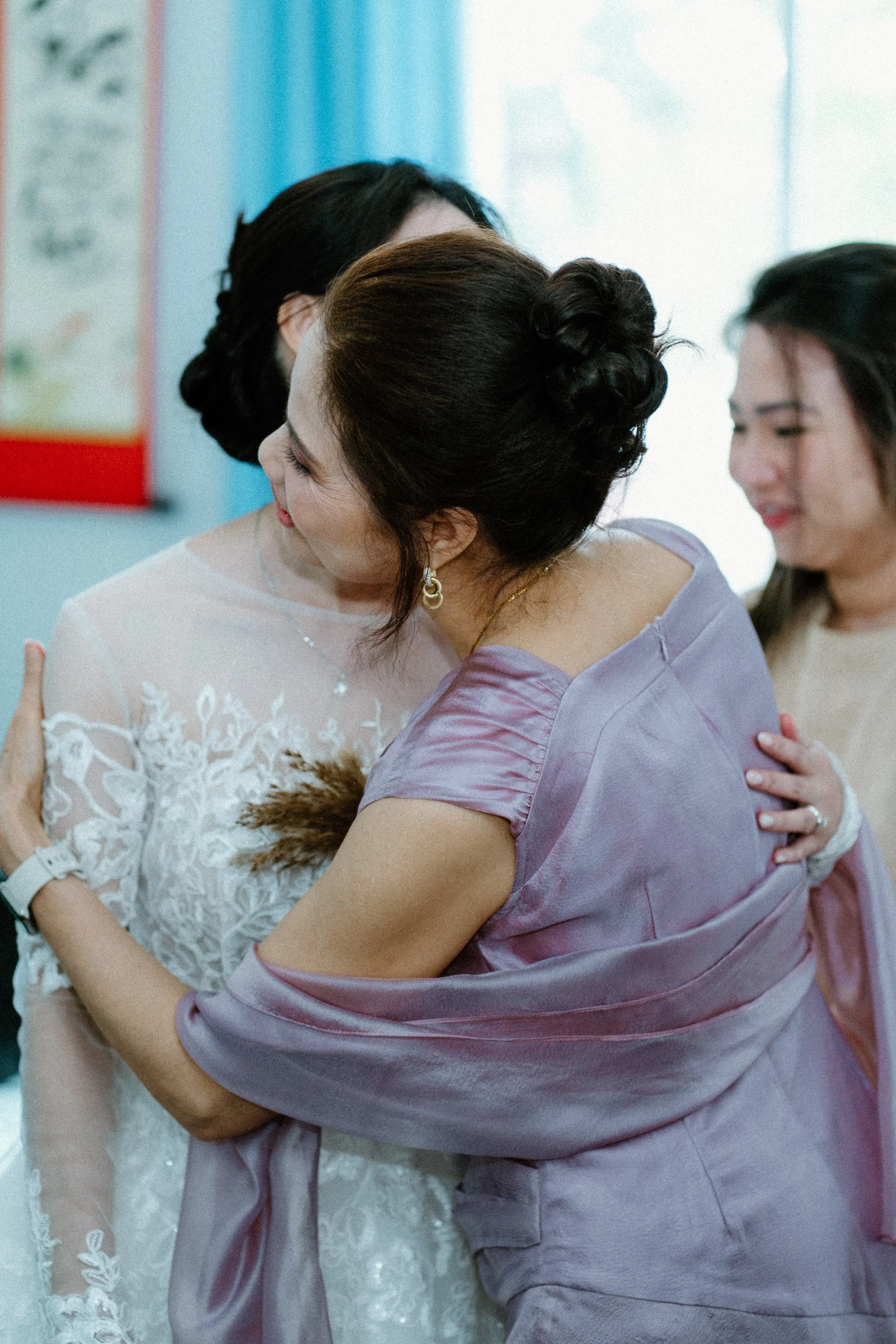Two women hugging, one in a white dress and the other in a lavender dress, with smiles.