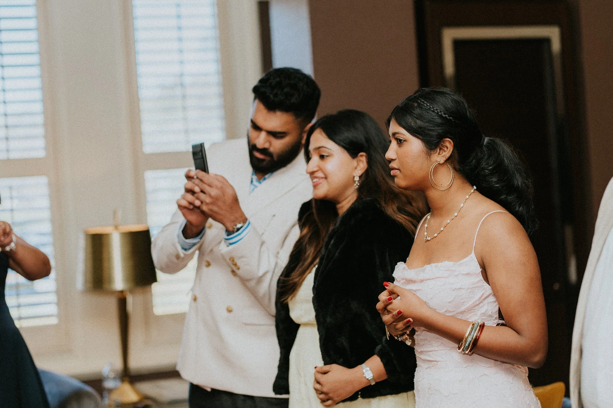 Three people standing side by side in a softly lit room, engaged in a moment of focus and attentiveness, with one person holding a smartphone.