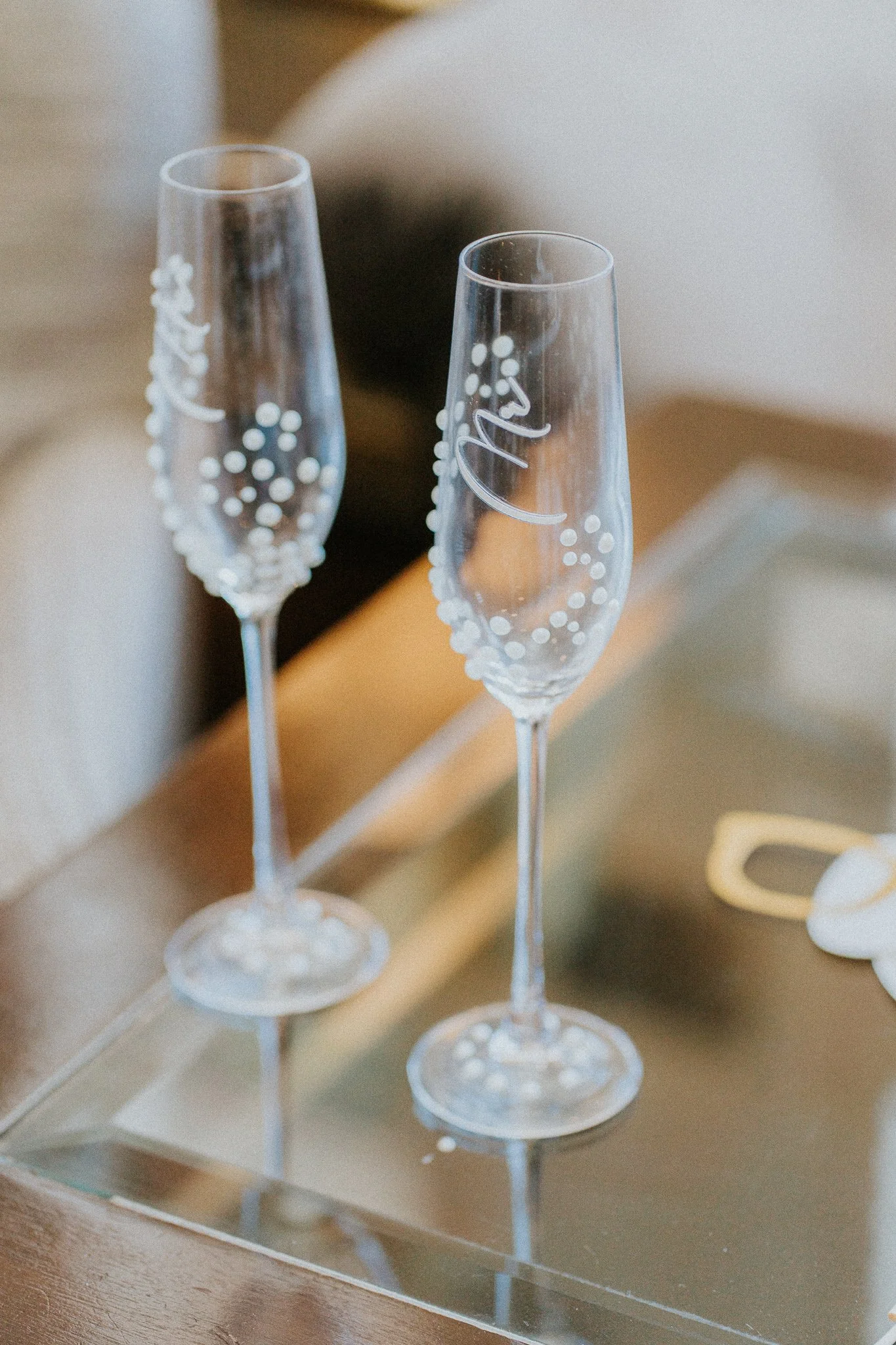 Three empty champagne glasses with white decorative dots and writing placed on a reflective surface.