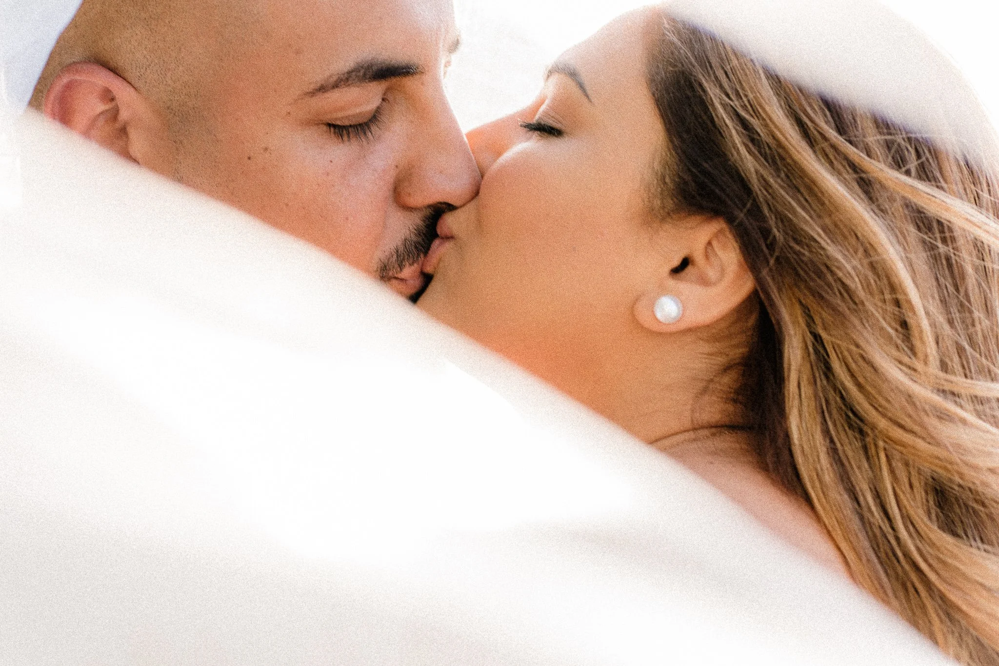 Close-up of a man and woman kissing, with the man having a shaved head and the woman wearing a pearl earring.