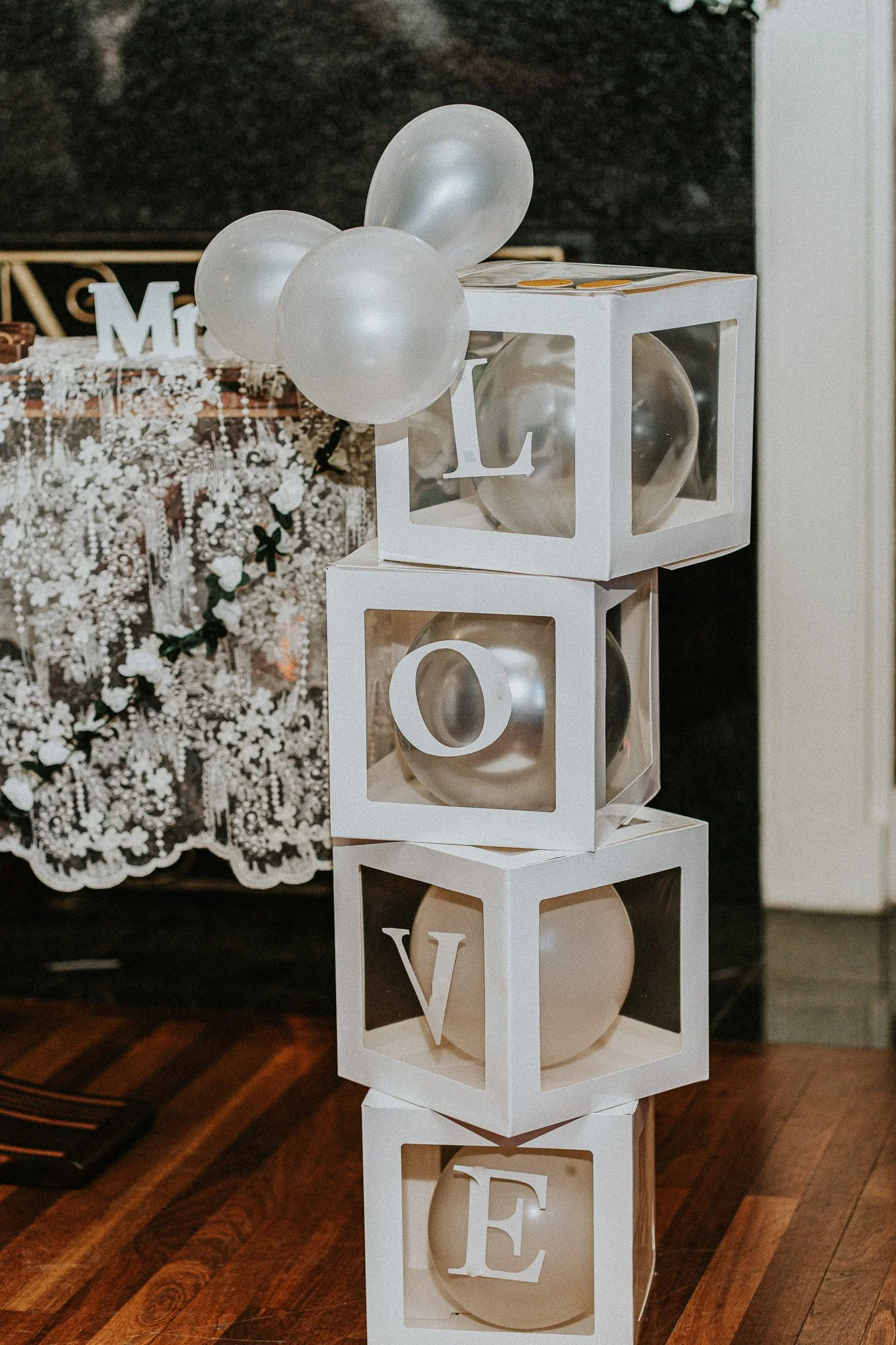 White decorative blocks stacked vertically with large cut-out letters spelling 'LOVE'. The blocks contain spherical balloons in black and white colors, placed in an indoor setting.