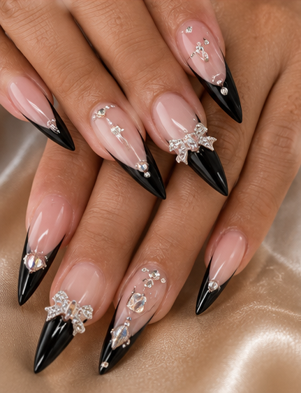 Close-up of manicured fingers with black-tipped, stiletto-shaped nails decorated with rhinestones and bows.