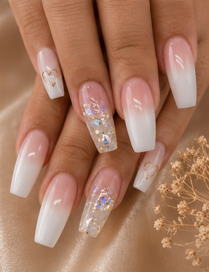 Close-up of manicured nails with a gradient white to pink design, decorated with small hearts and iridescent glitter, against a satin background with small dried flowers.