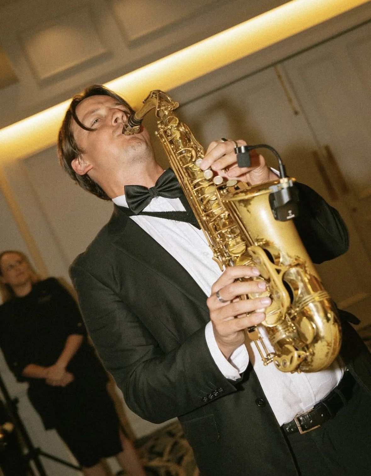 A man in a tuxedo playing a gold saxophone at a wedding for the dance floor.