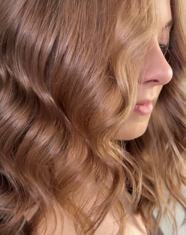 Close-up of a woman with wavy red hair and light skin, her face turned to the side.