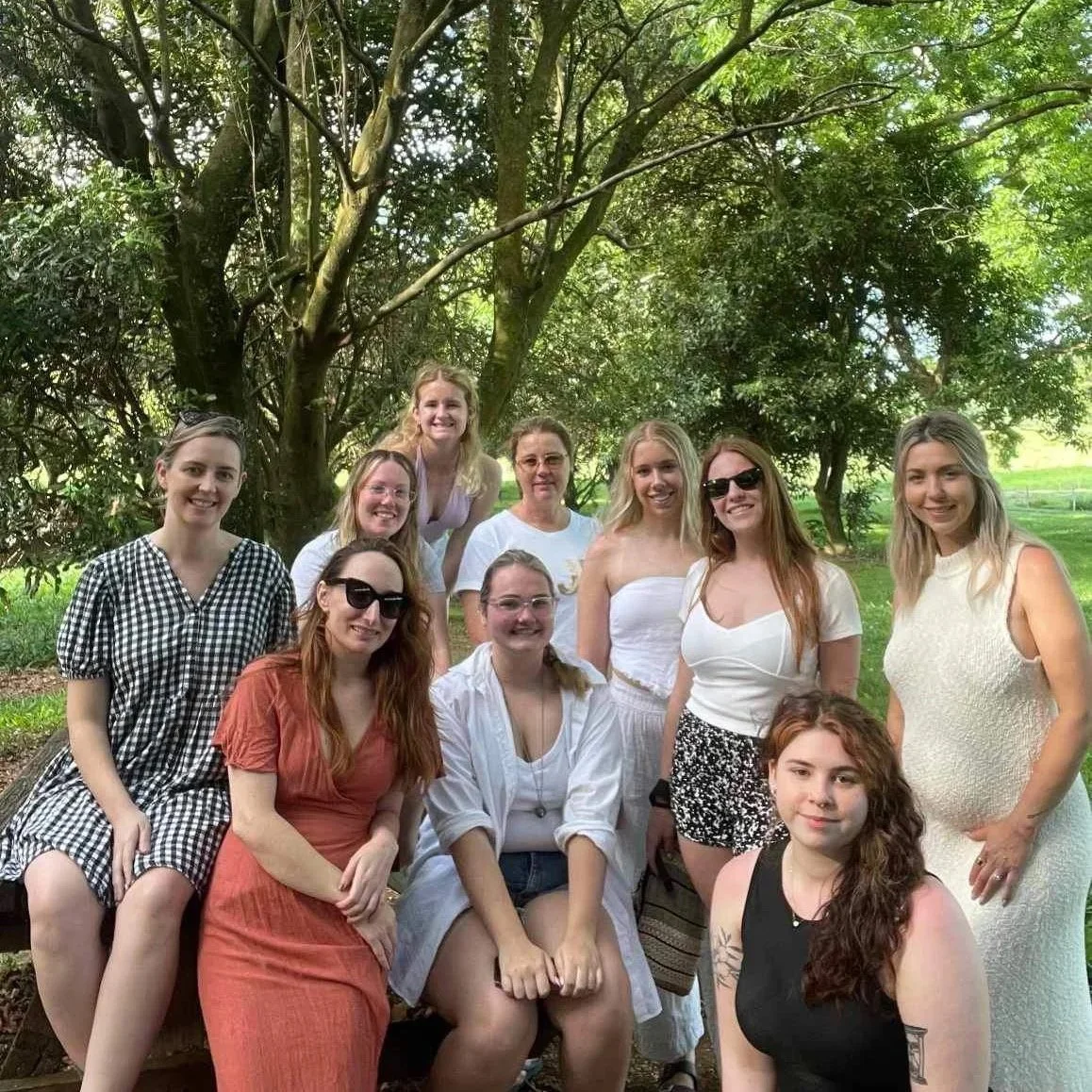 Group of ten women gathered outdoors under trees, smiling for a photo.