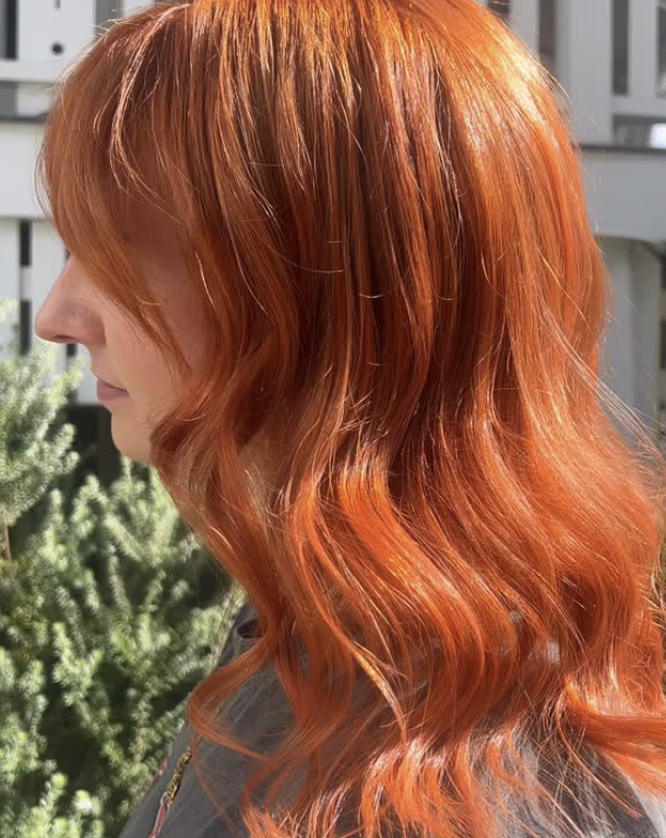 Side profile of a woman with long, wavy, bright orange hair.