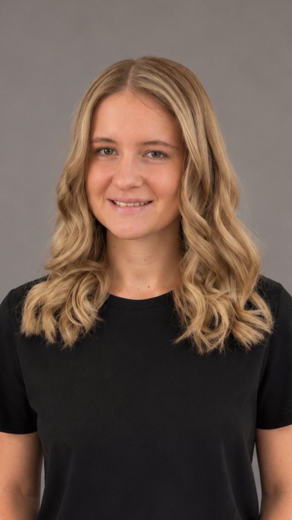 A young woman with wavy blonde hair wearing a black shirt, smiling in front of a gray background.