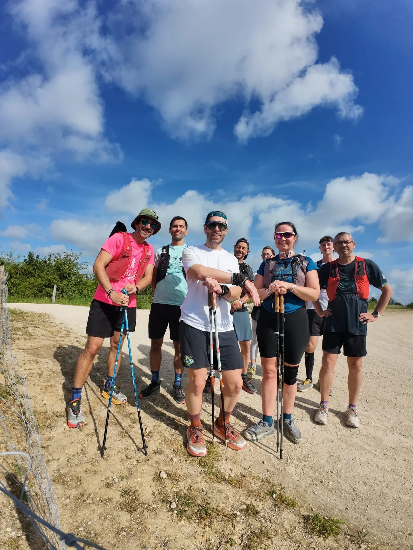 Groupe de trail en plein air sous un ciel bleu , certains portant des bâtons de marche et des vêtements de sport technique