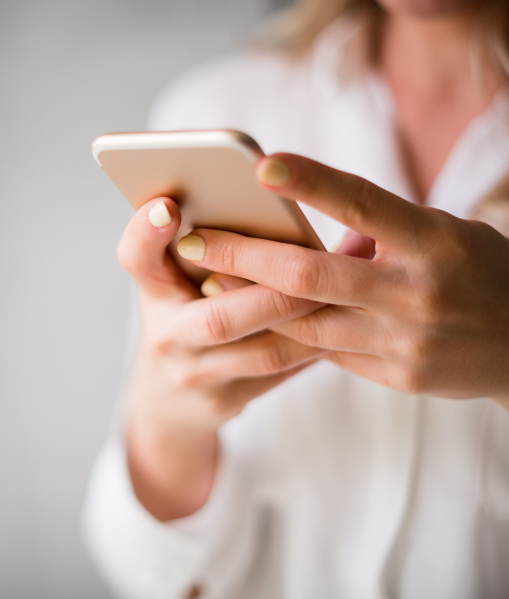 Close-up of a person's hand holding a smartphone, with focus on their thumb and fingers, blurred background.