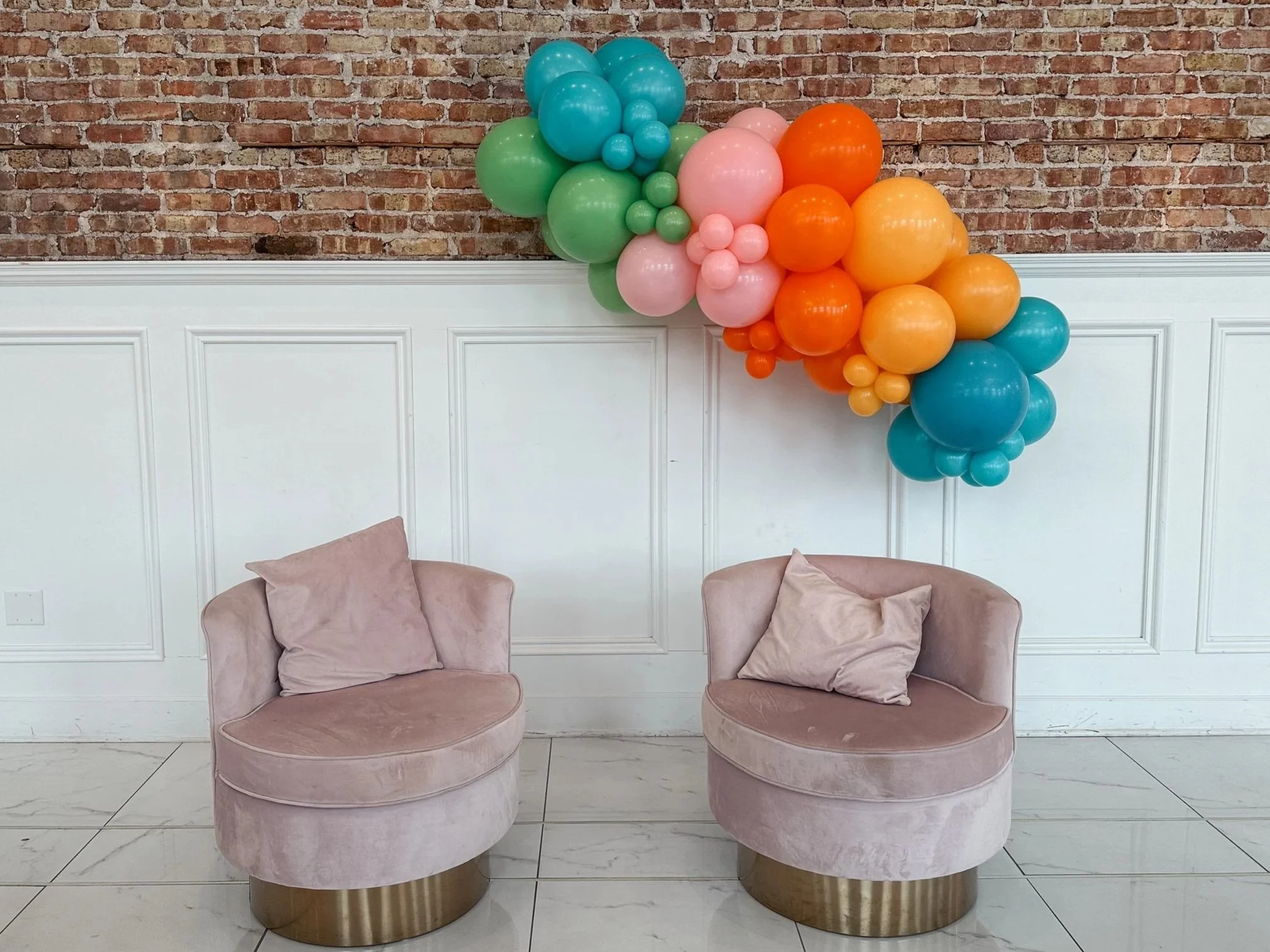 Colorful organic balloon garland in teal, orange, pink and green. hues hanging on the brick wall.