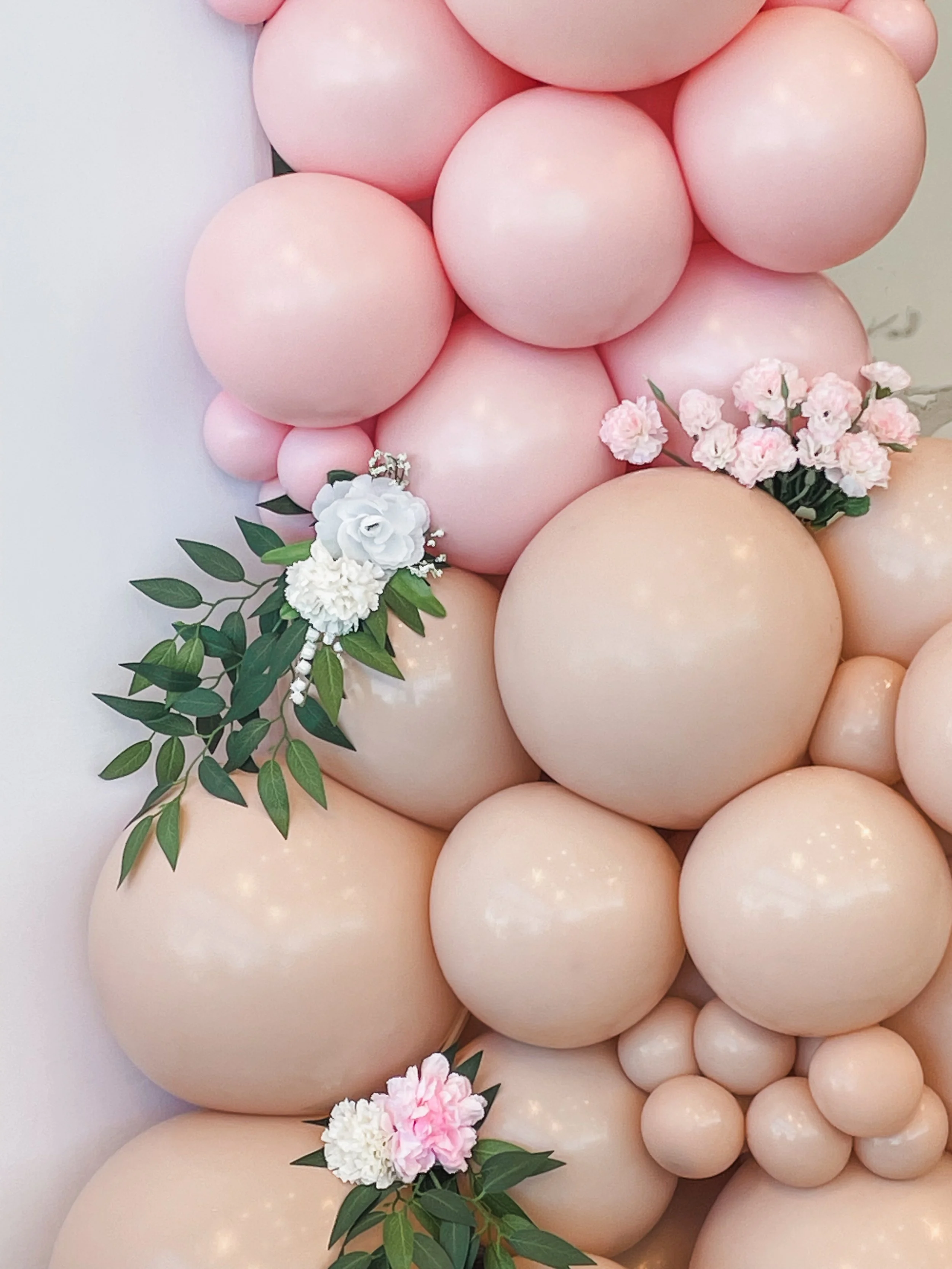 A collection of pink and beige balloons decorated with white and pink flowers and green leaves.