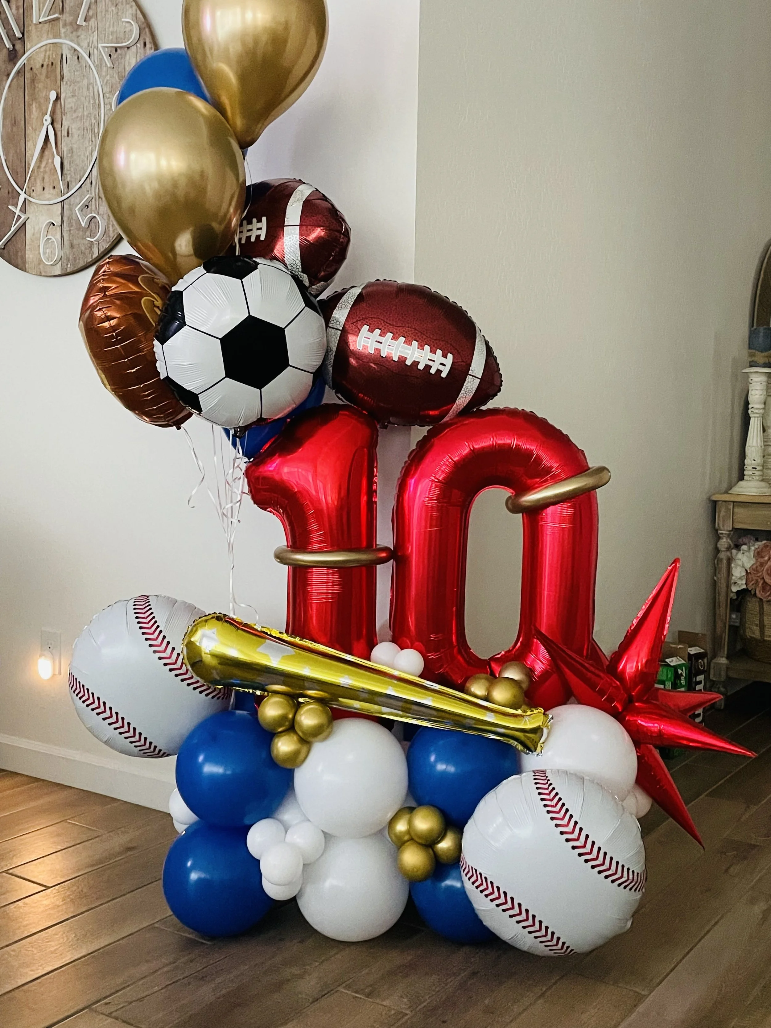 A balloon display with balloons shaped like footballs, baseballs, a trophy, and various round balloons in red, white, blue, black, and gold colors, 10th Birthday balloon bouquet
