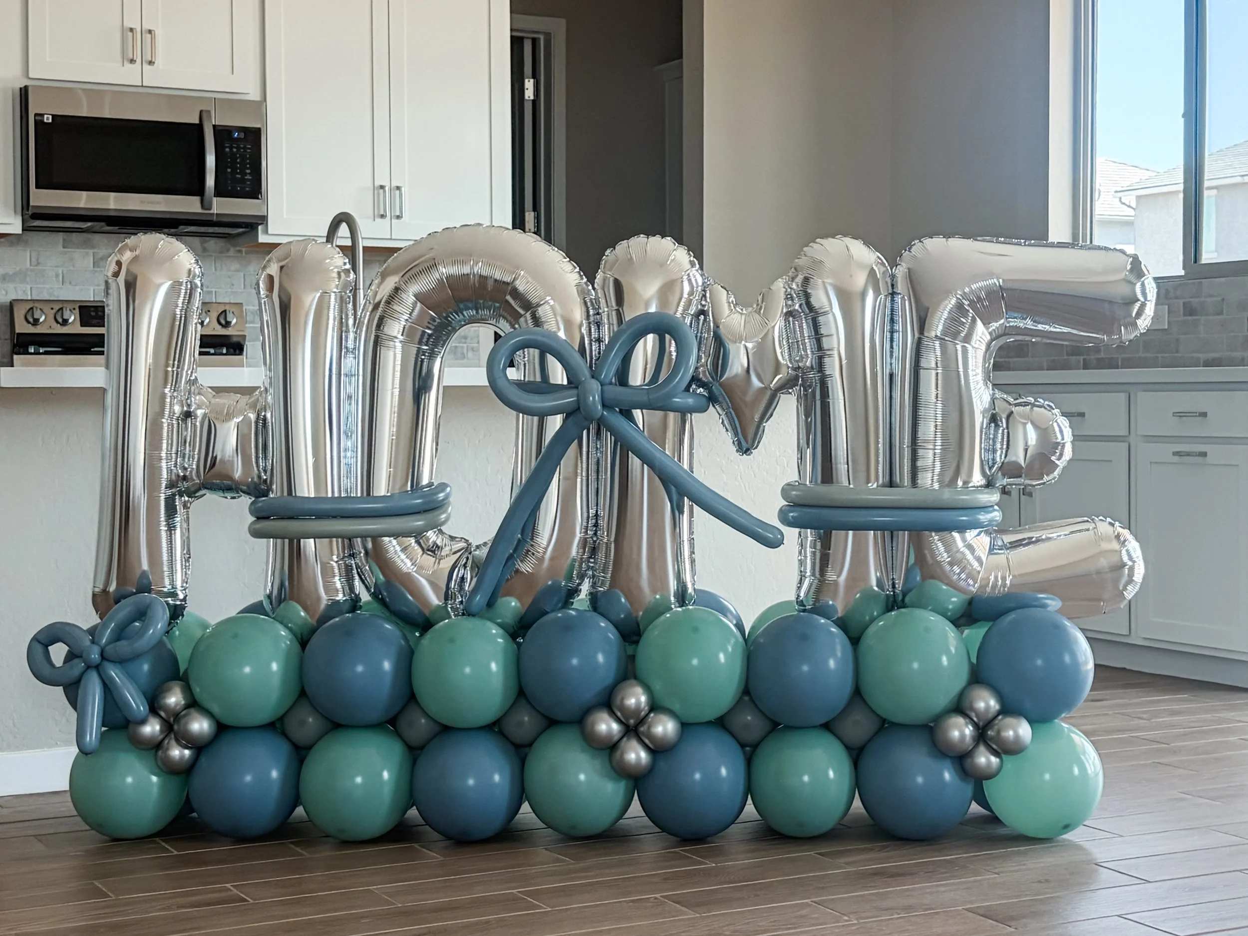 Balloon arrangement spelling 'HOME' with blue and silver balloons.  BALLOON bouquet for new homeowners. 