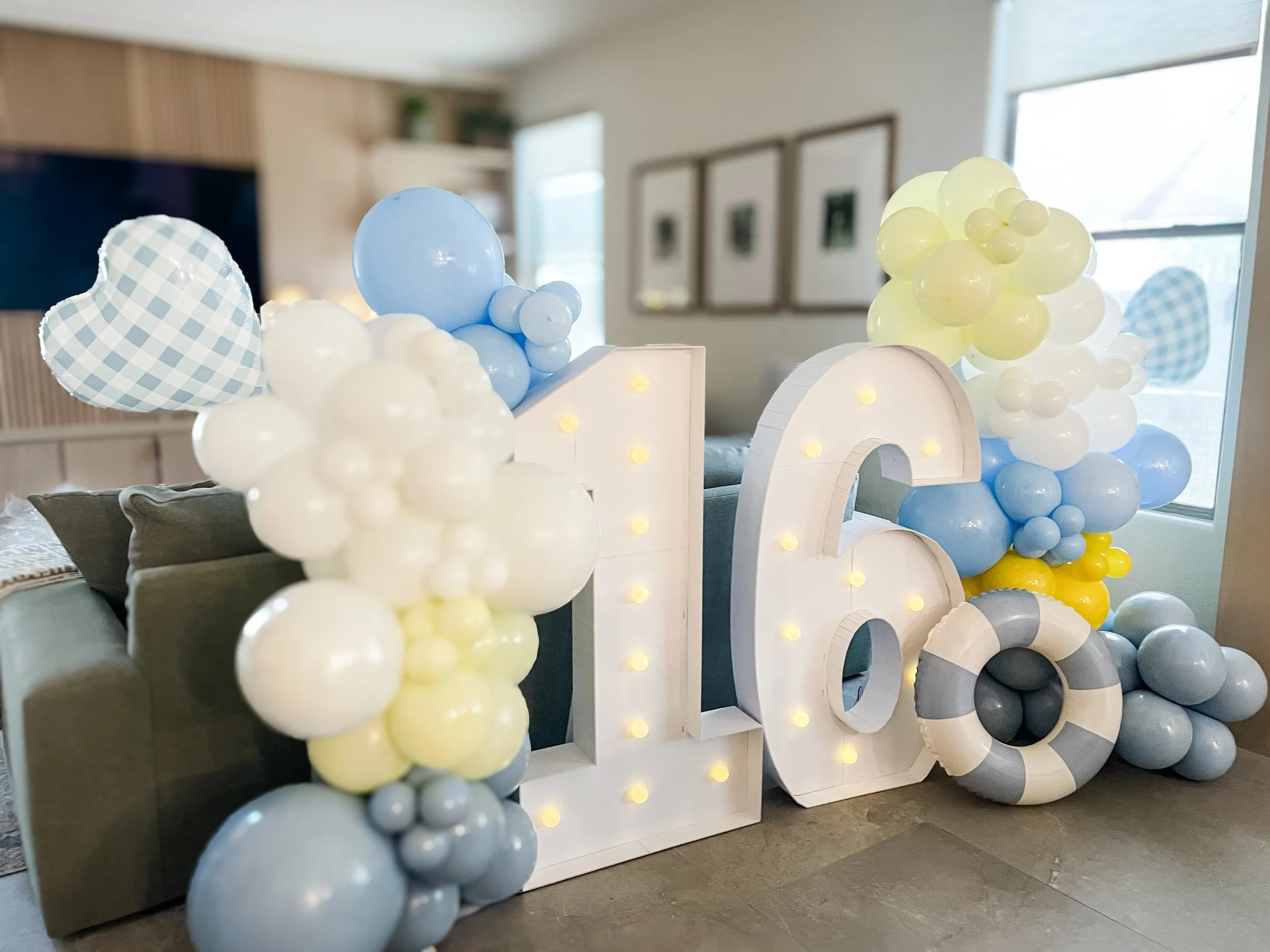 Decorative balloon arch with white, yellow, gray, and blue balloons surrounding baloon marquees . 16'th Birthday balloons