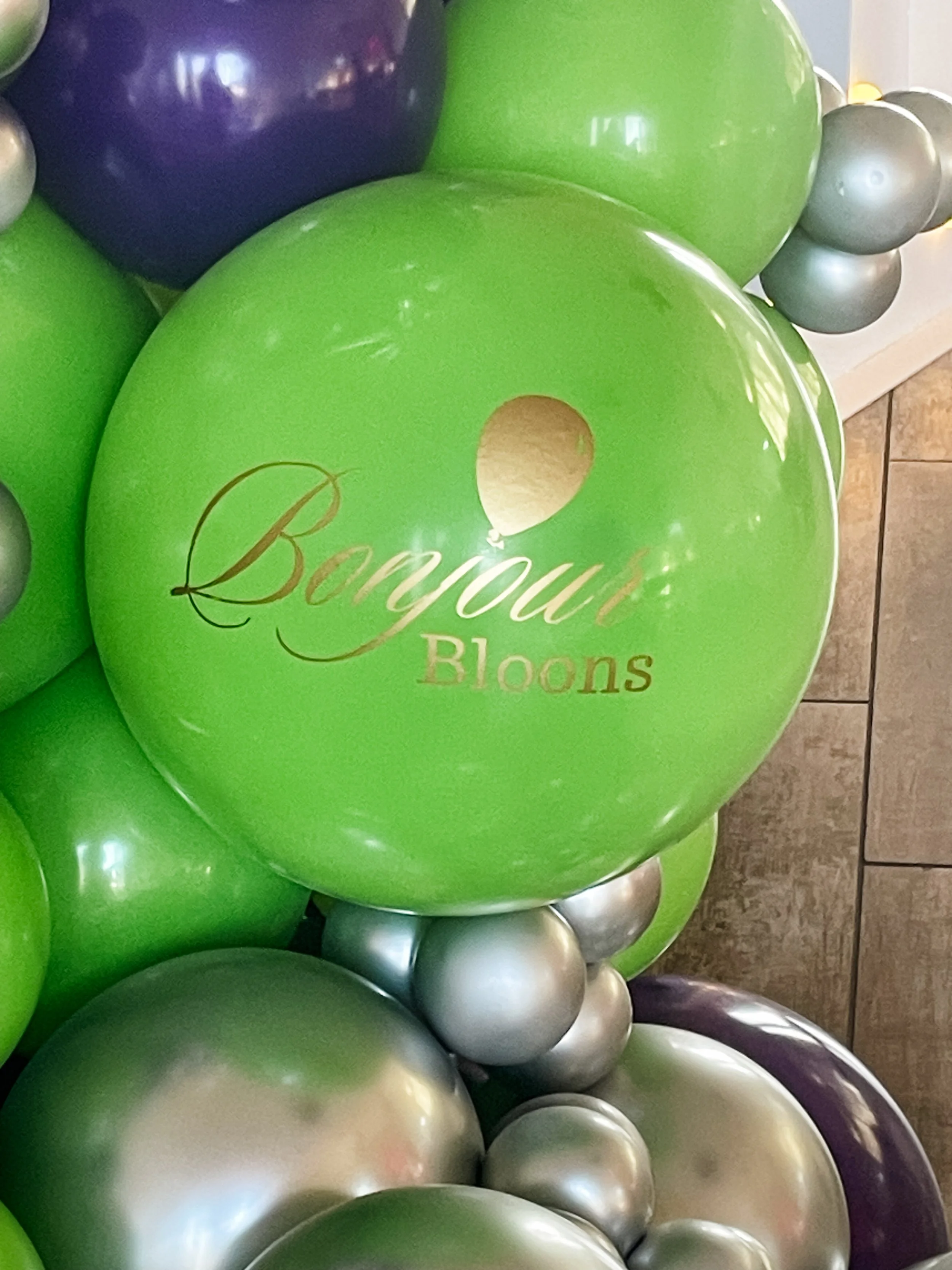 Close-up of green, purple, and silver balloons with the words 'bonjour Bloons' printed on the green balloon.