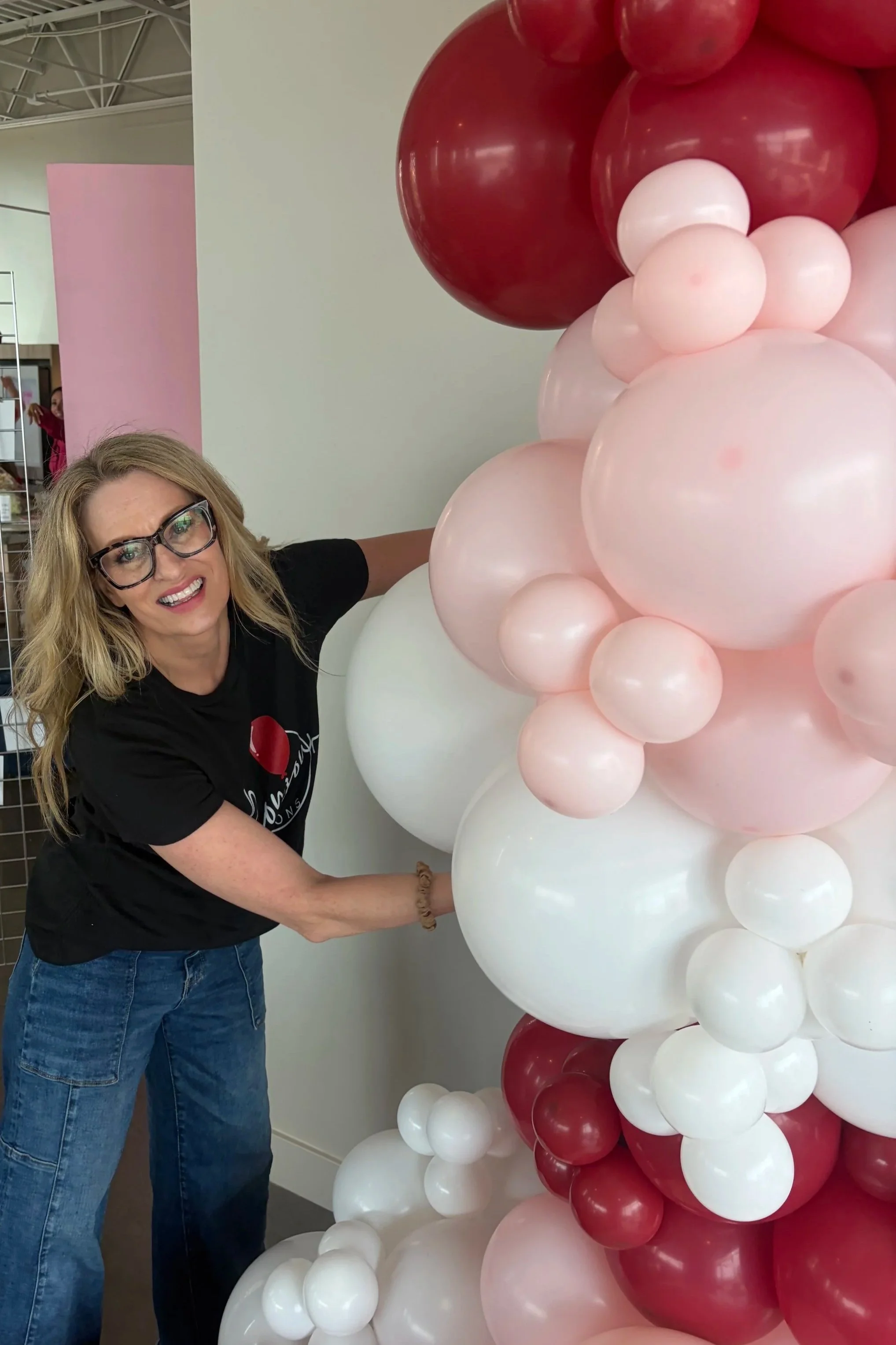 Jeanee of Bonjour Bloons assembling a pink, red and white balloon installation.