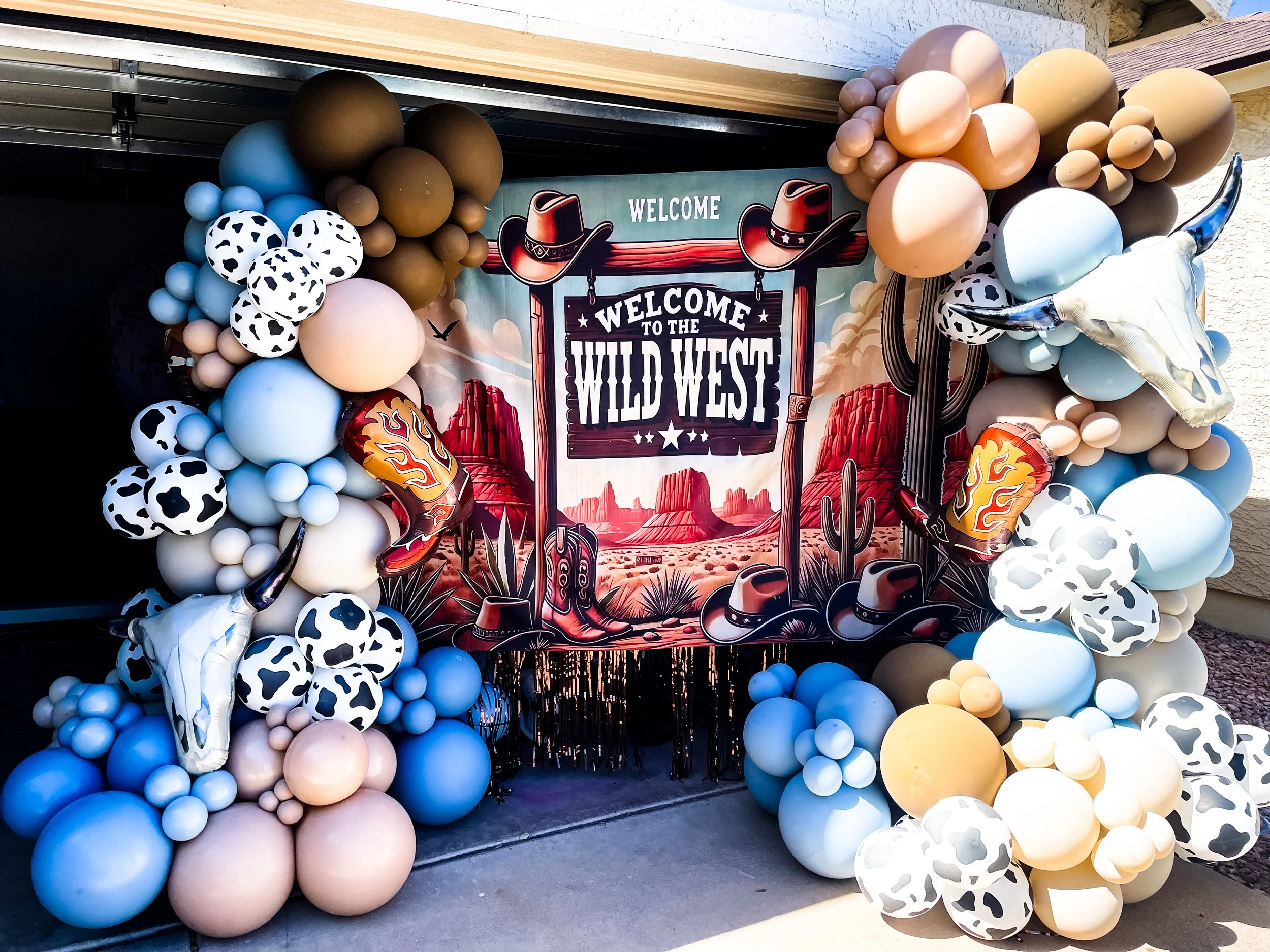 Balloon arch with a western themed sign that reads 'Welcome to the Wild West' and cowboy hats, cowboy boots, and desert landscape images.