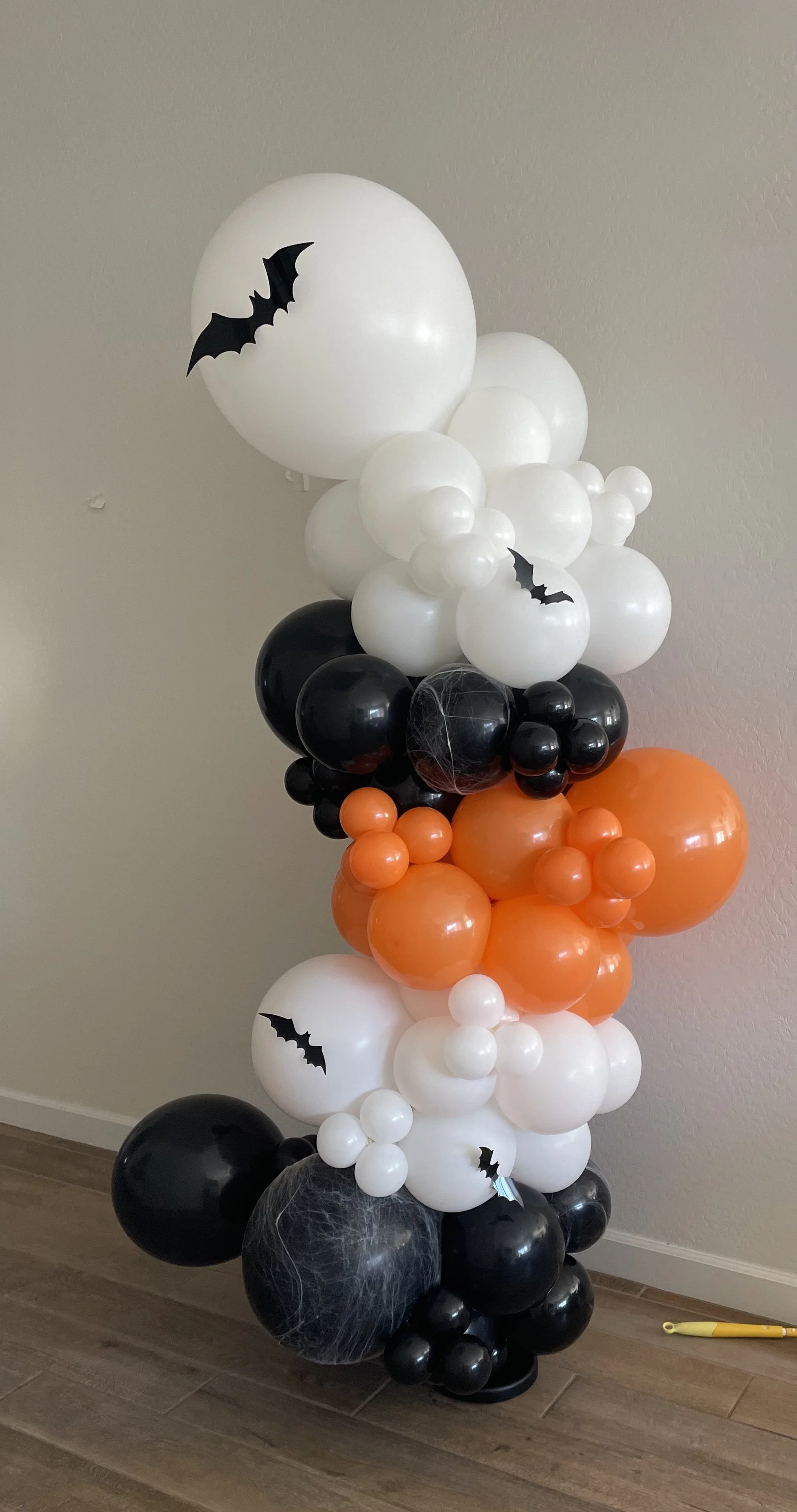 A Halloween-themed balloon column with black, white, and orange balloons, decorated with bat stickers and faux spider webs.