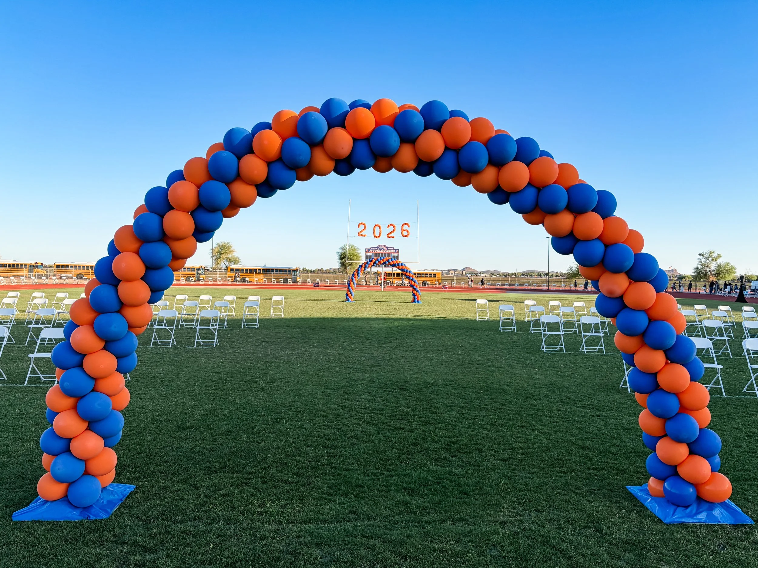 Colorful balloon arch with orange and blue balloons on a sports field displaying '2026'.  Graduation Ceremony Balloons