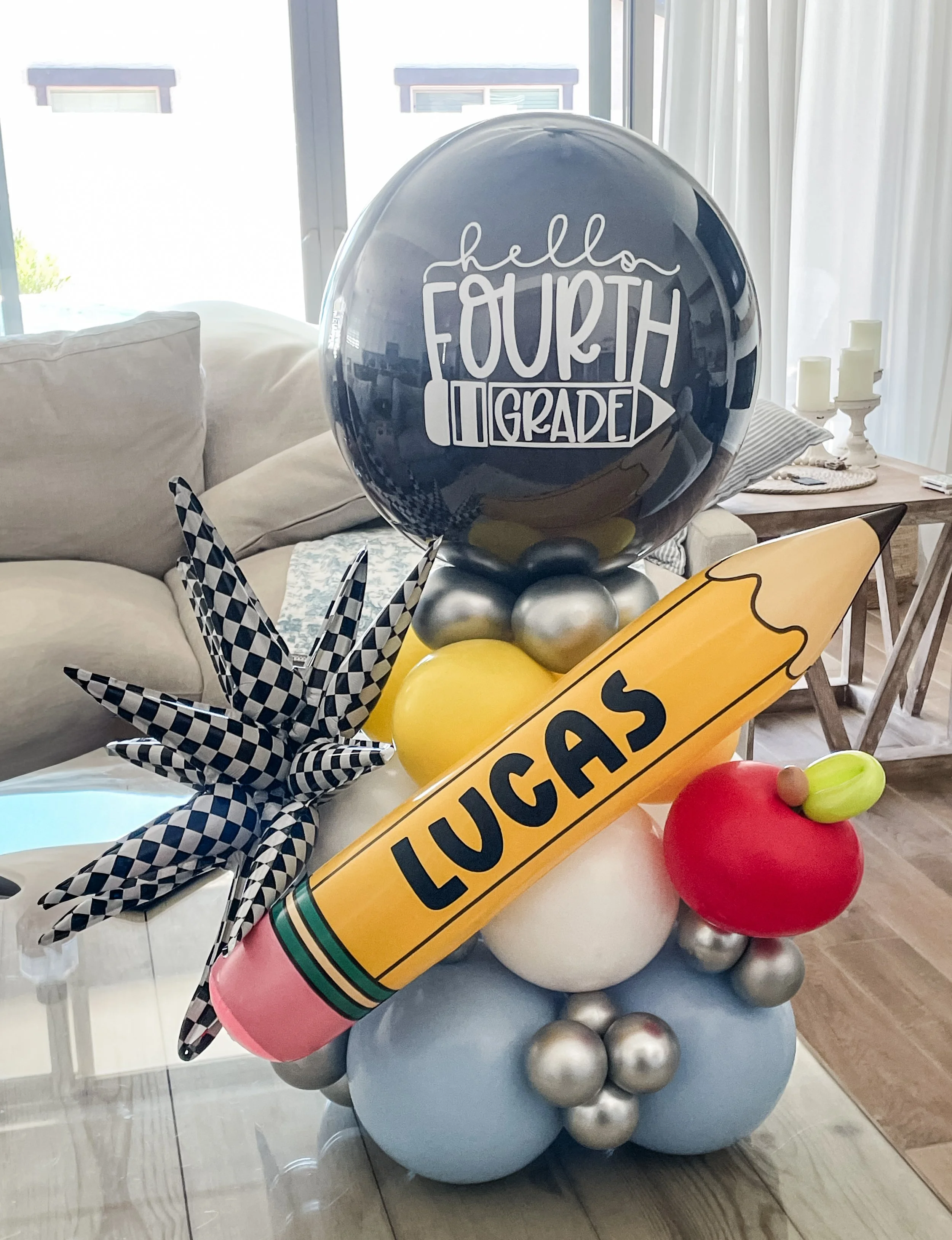 Decorative back-to-school ballon stack with a large black balloon with white lettering saying 'hello fourth grade,' surrounded by colorful balloons and decorative elements.