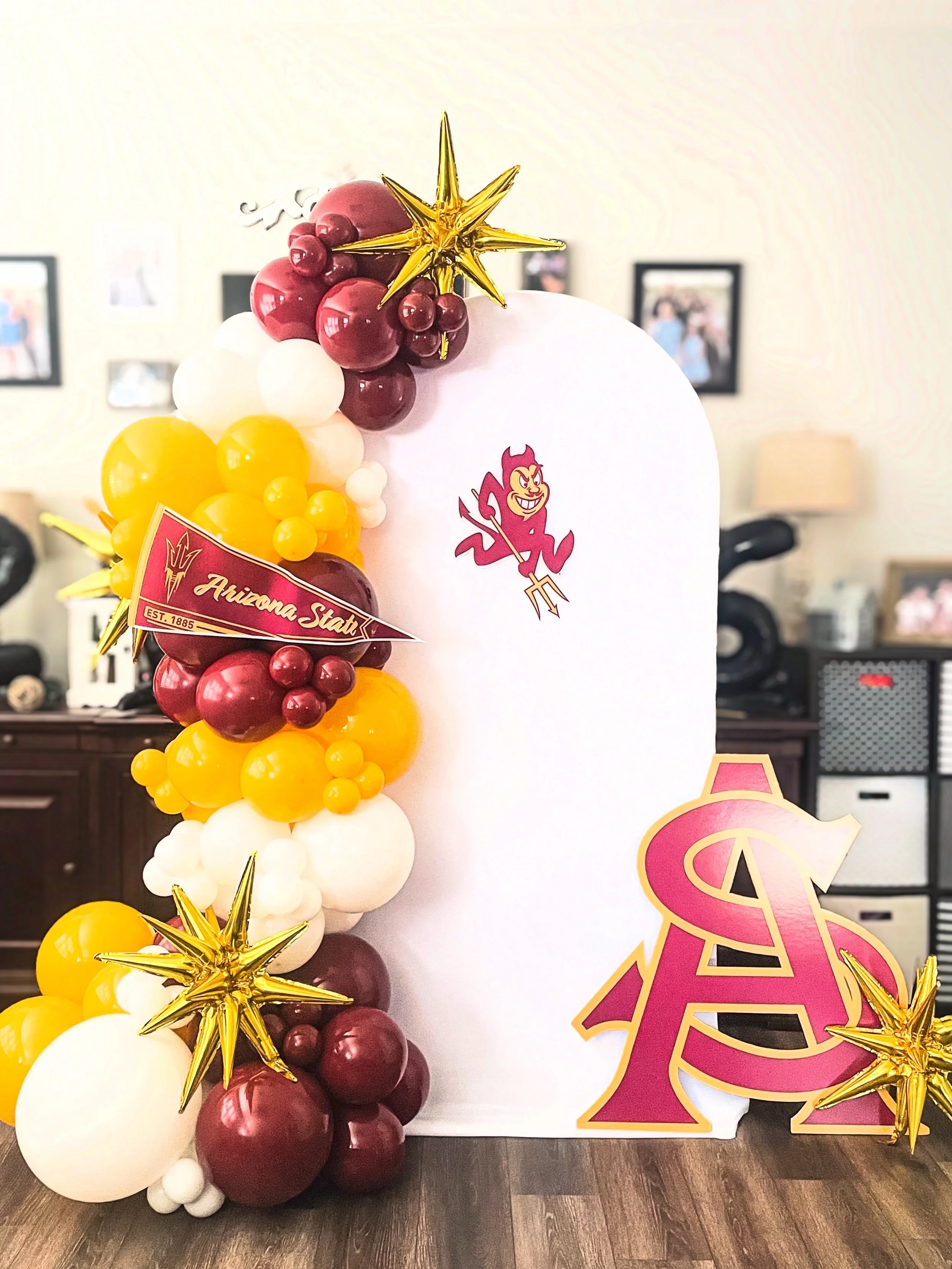 Decorative balloon arrangement featuring maroon, white, and yellow balloons with gold star accents, and a large structure with the Arizona State University logo.
