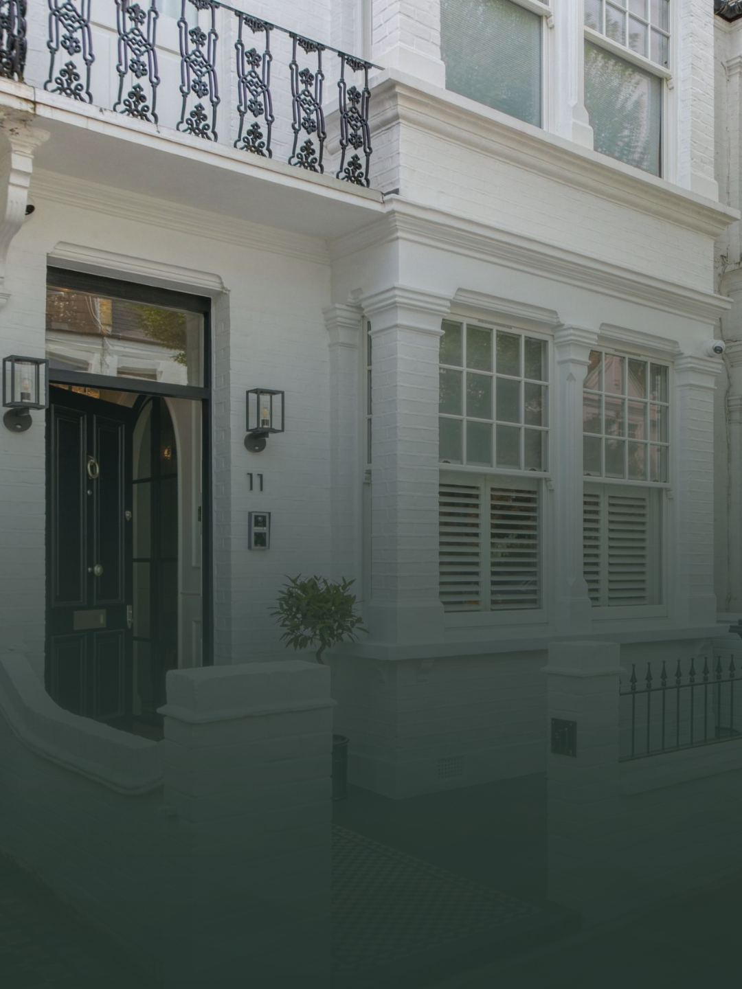 White brick townhouse with black front door, decorative black iron balcony, and multiple large windows with shutters.