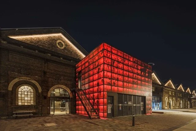 Night view of a historic train station with a modern, red illuminated glass addition.