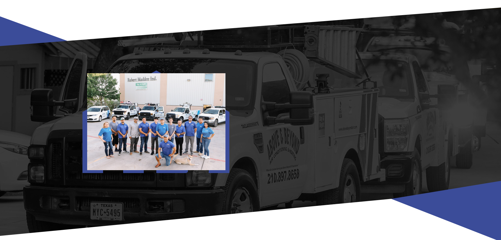 Group photo of team members standing in front of trucks outside of a building, some wearing blue shirts, with one person kneeling and a dog laying on the ground nearby.