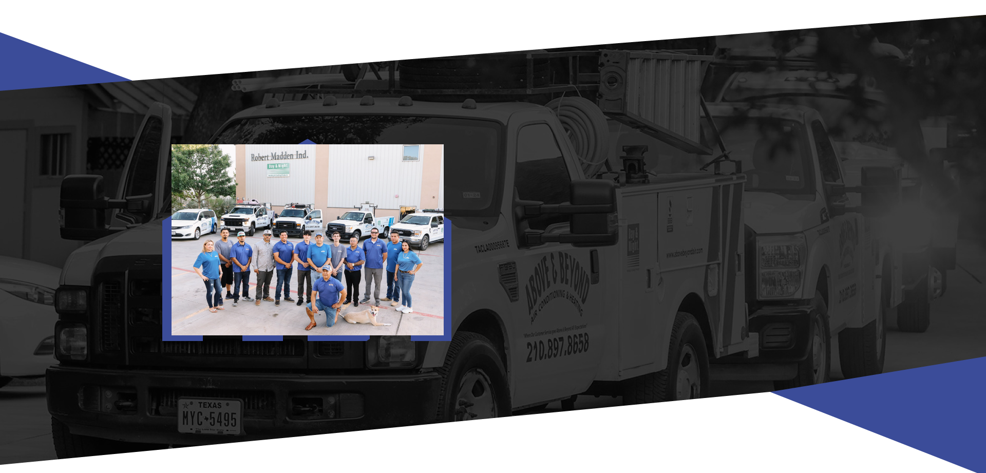 Group photo of team members standing in front of trucks outside of a building, some wearing blue shirts, with one person kneeling and a dog laying on the ground nearby.